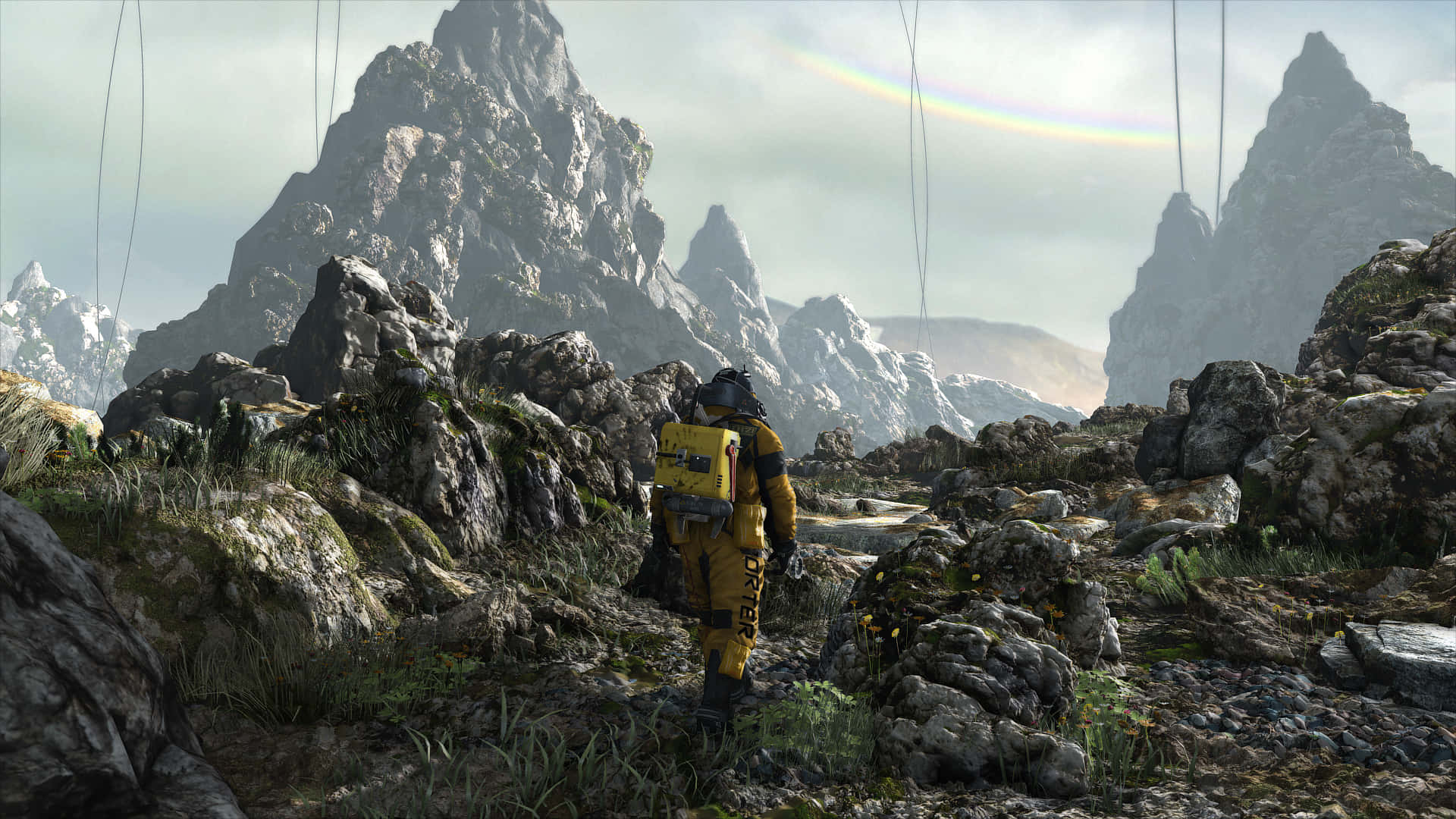 HD Death Stranding 桌布 壁紙 — 一個孤獨的太空人穿著黃色太空衣，在微弱的彩虹下走過岩石外星景觀。
