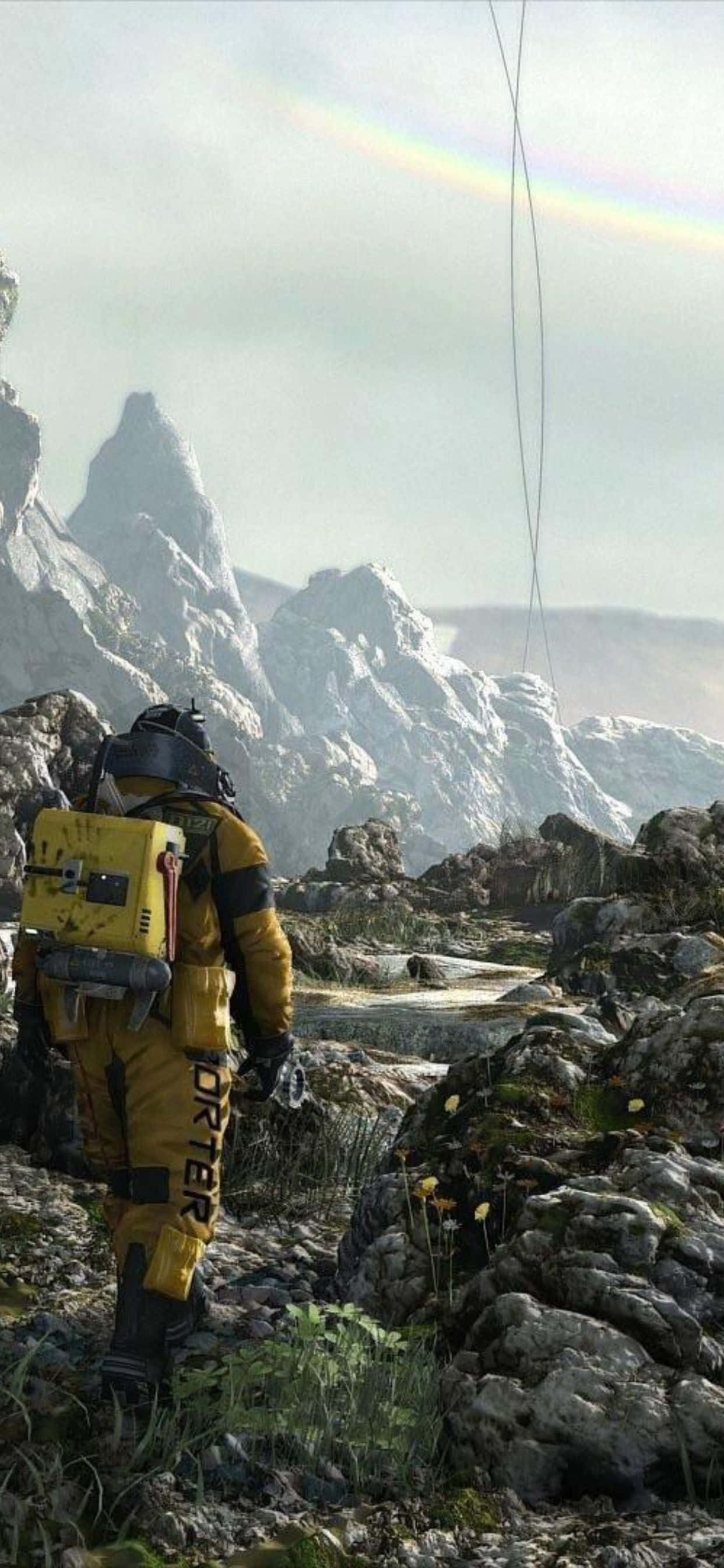 iPhone Xs Max Death Stranding 桌布 壁紙 — 一個孤獨的太空人穿著黃色太空衣，在微弱的彩虹下走過岩石密布的外星景觀。