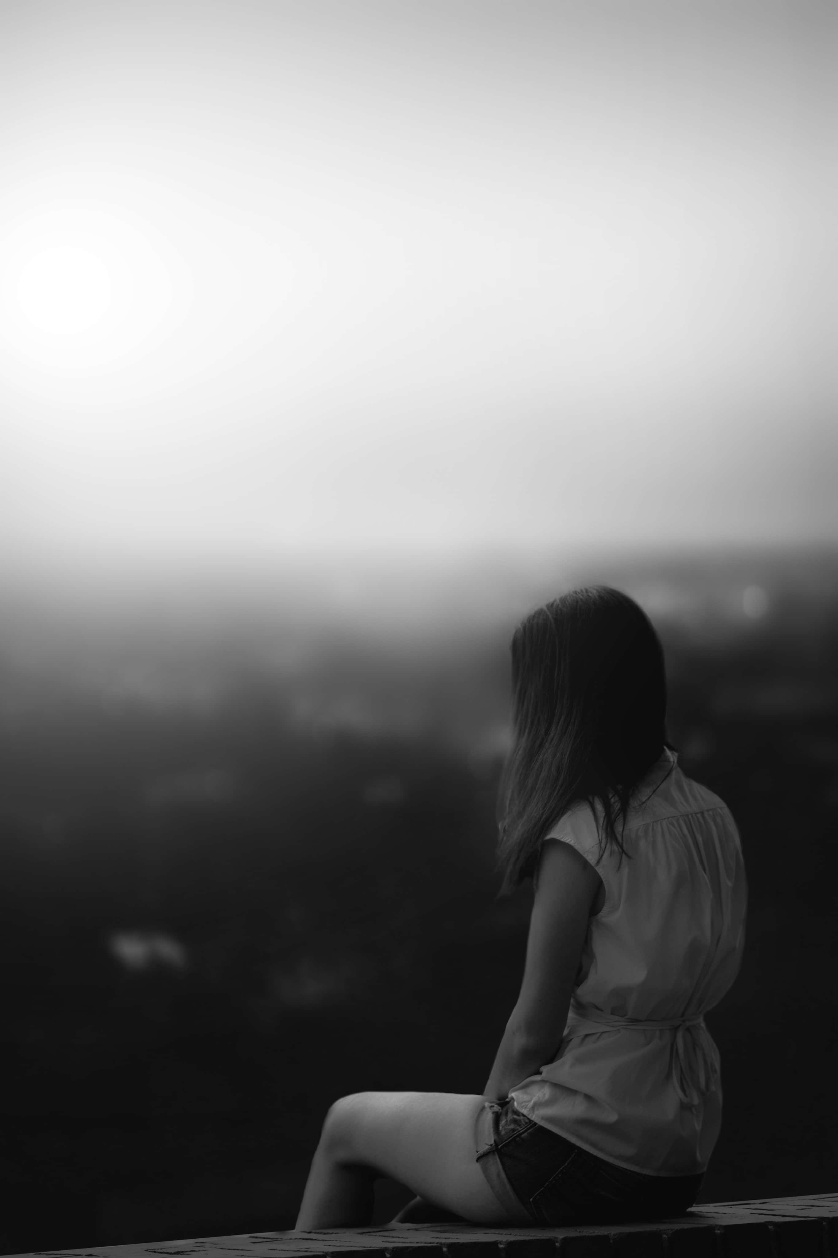 Woman 桌布 壁紙 — 一個孤獨的女人以單色剪影坐著，眺望黎明時分朦朧的城市景觀。