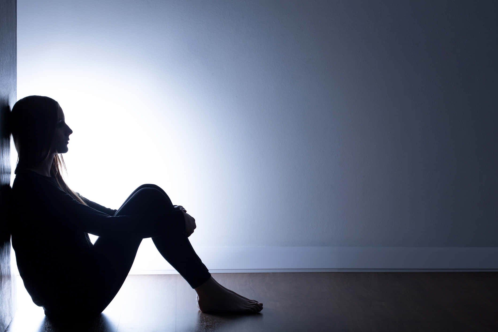 Depressed 桌布 壁紙 — 一個孤獨的女人坐在明亮的牆壁前，形成剪影，沐浴在柔和背光中，傳達出安靜的孤獨感。