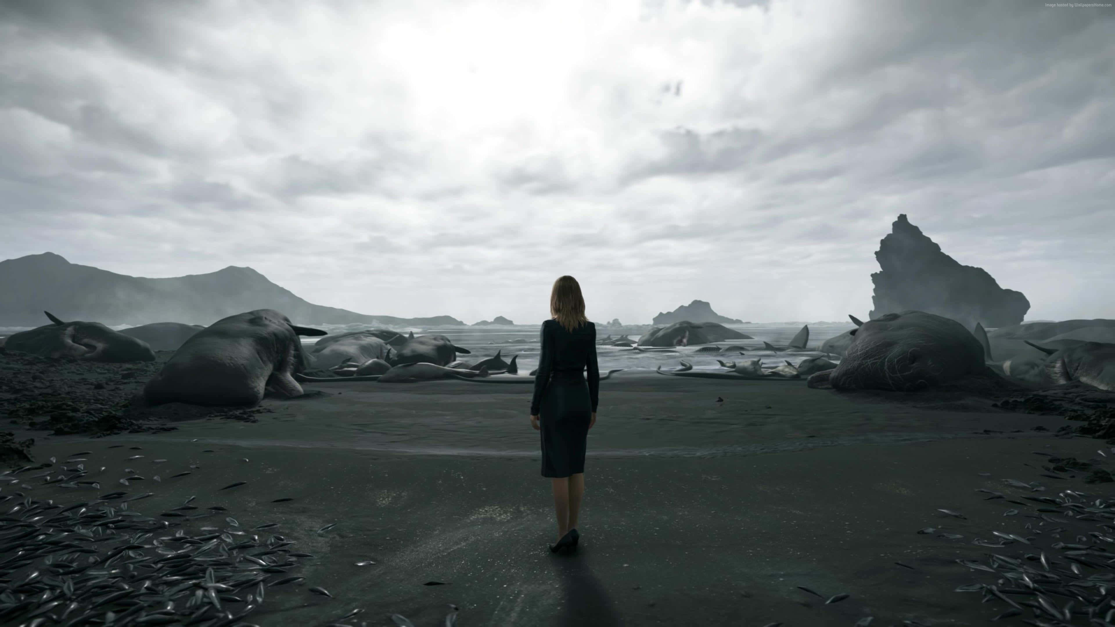 Death Stranding Pc 桌布 壁紙 — 一個孤獨的女人穿著深色連衣裙，站在荒涼的黑沙灘上，凝視著陰天天空下散落的死鯨。