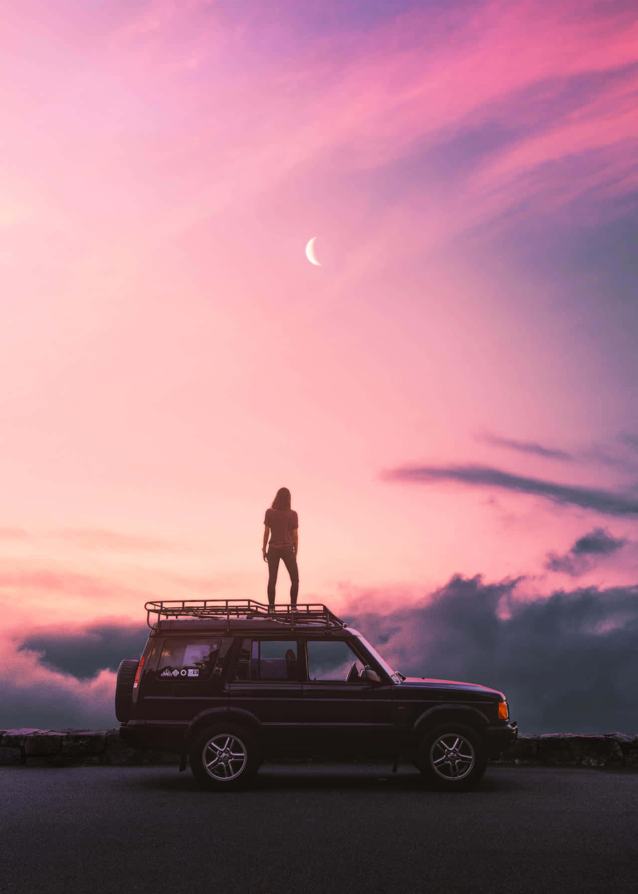 Vibes 桌布 壁紙 — 一個孤獨的女人站在一輛停泊的SUV車頂上，背景是夢幻的粉紅和紫色暮色天空，掛著一彎新月。
