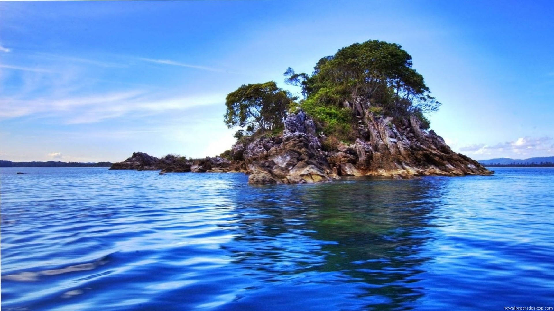 1920x1080 高畫質自然 桌布 壁紙 — 一個孤獨的岩石島嶼，長滿茂密的綠樹，從湛藍的海水中升起，天空晴朗。