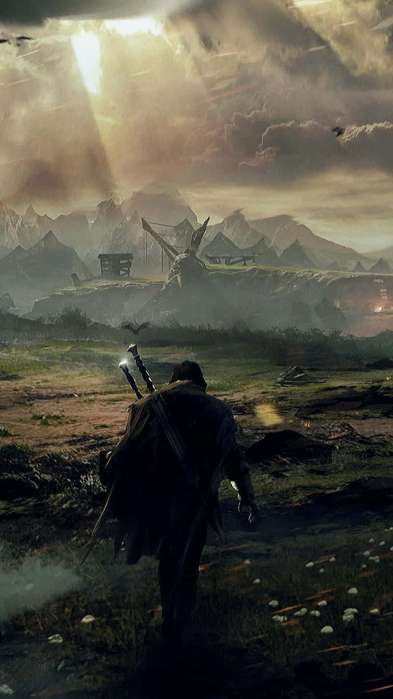 Shadow Of Mordor 桌布 壁紙 — 一個孤獨的戰士背著劍，穿過霧氣瀰漫的田野，走向遠方的山脈，天空戲劇性地陽光明媚。