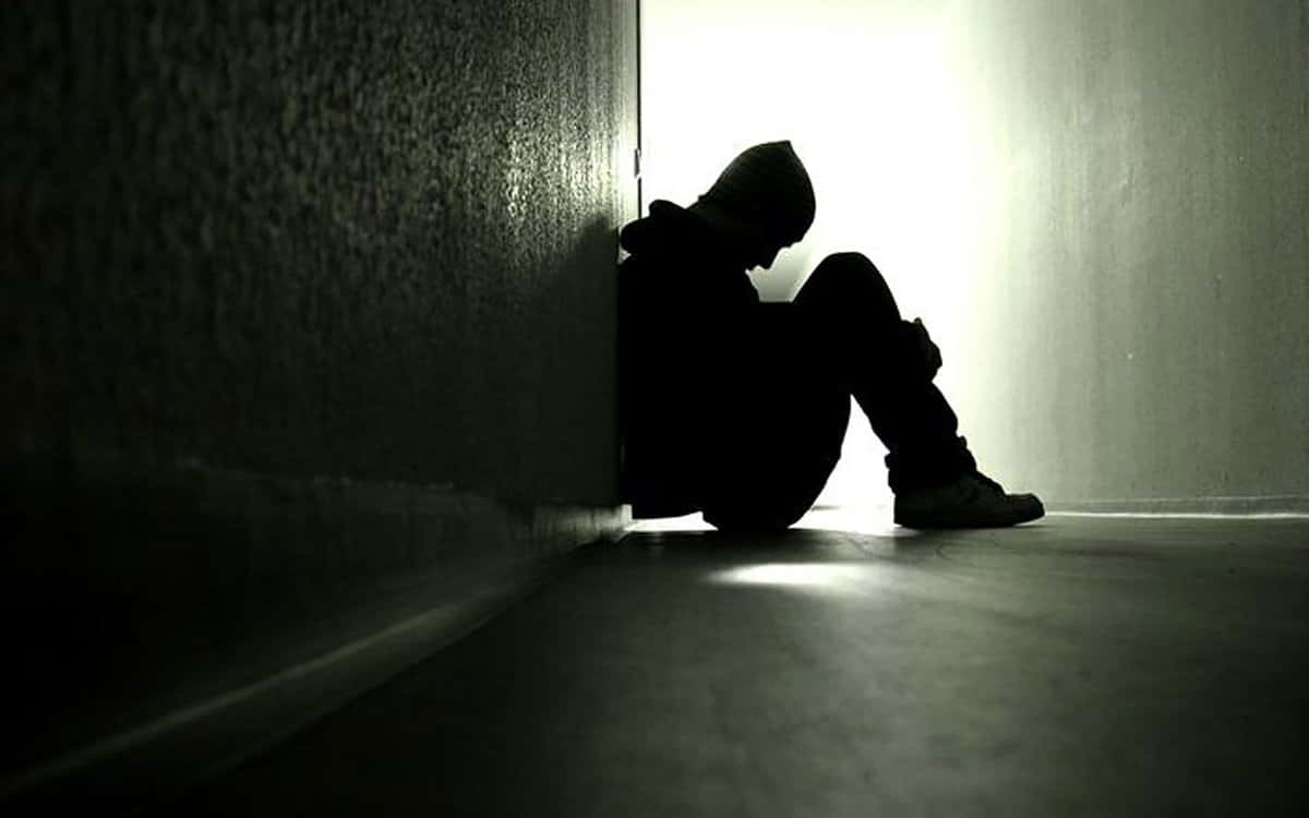 Lonely 桌布 壁紙 — 一個孤獨的戴兜帽身影蜷縮在陰暗的巷子角落，沐浴在強烈的背光中。