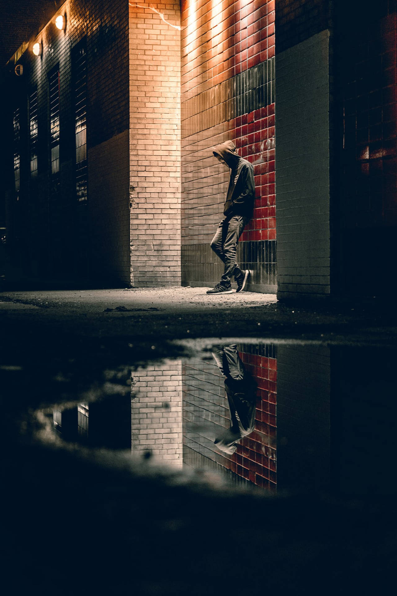 穿連帽衫的人靠著磚牆，夜晚水坑倒影 — 憂鬱男孩 壁紙