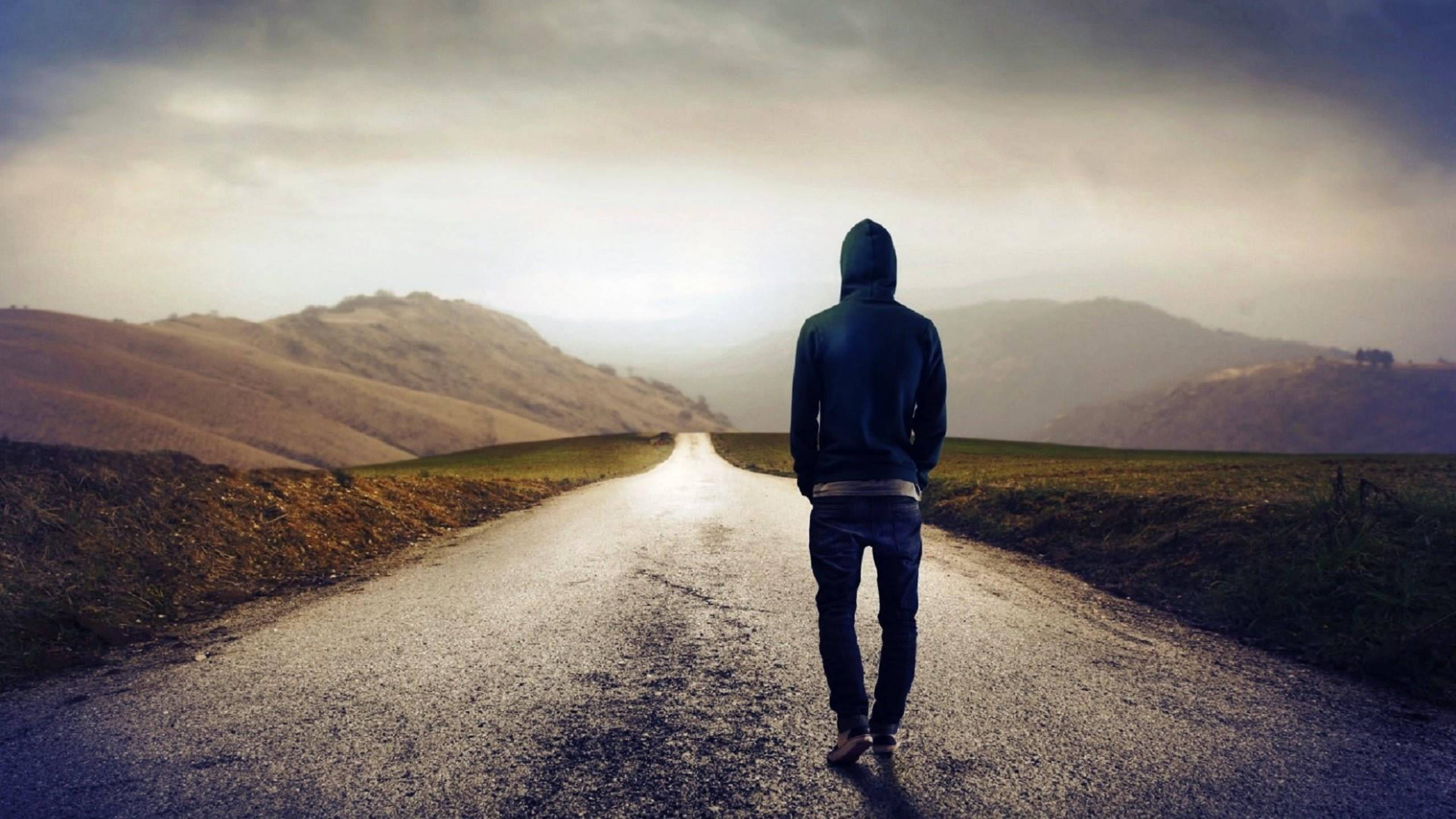 Alone 桌布 壁紙 — 一個孤獨的戴帽人影在潮濕的道路上走向遠山，天空陰沉多雲。