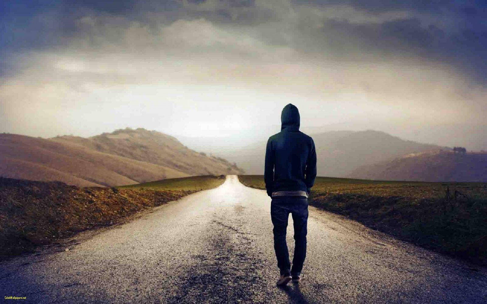 walking away 桌布 壁紙 — 一個孤獨的戴帽人影在陰沉多雲的天空下，沿著濕漉漉的道路走向遠方的山丘。