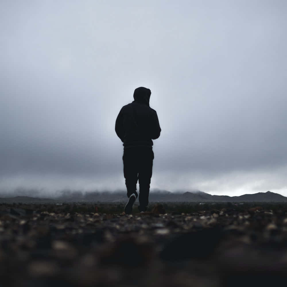 Lonely 桌布 壁紙 — 一個孤獨的戴帽人影在霧氣瀰漫的岩石平原上走遠，天空灰濛濛，遠方有山丘。