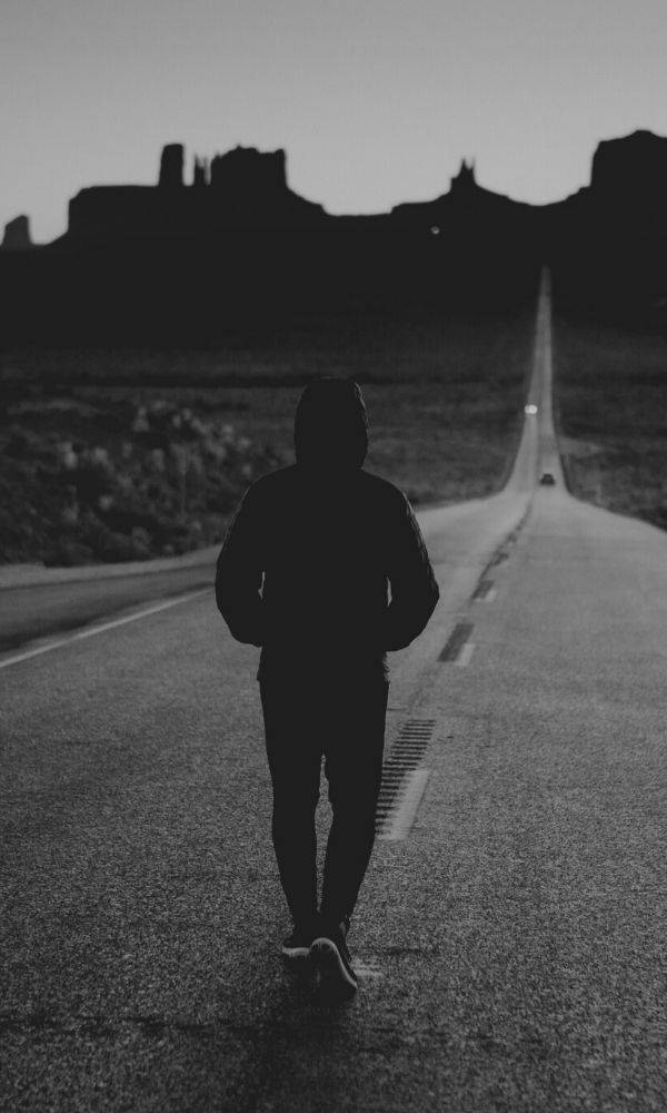 一個人在黃昏時沿著漫長沙漠道路行走的剪影。 — 單身男孩 壁紙