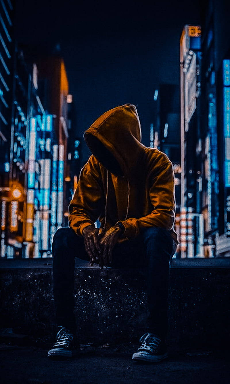 一個穿連帽衫的人夜晚獨自坐在城市窗台上，下方是發光的霓虹燈。 — 單身男孩 壁紙