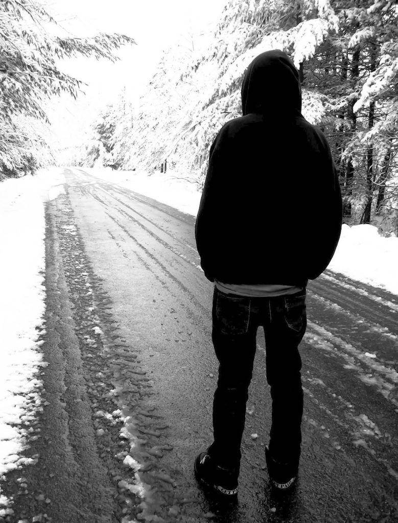 穿連帽衫的人獨自站在冬季森林的積雪道路上。