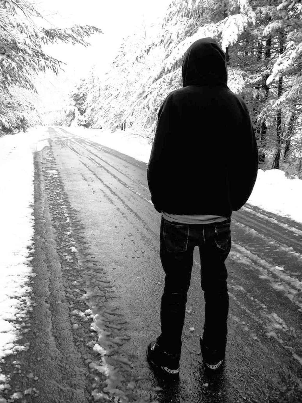 雪 桌布 壁紙 — 一個孤獨的戴帽人物站在一條被雪覆蓋的道路上，兩旁是積雪的樹木，以單色呈現。
