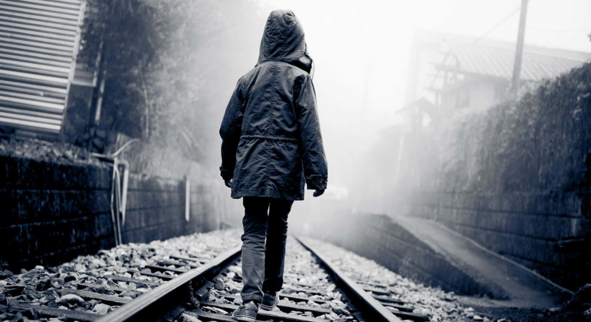 Alone 桌布 壁紙 — 一個孤獨的戴帽身影沿著霧氣瀰漫的鐵軌走遠，兩旁是石牆和模糊的建築物。