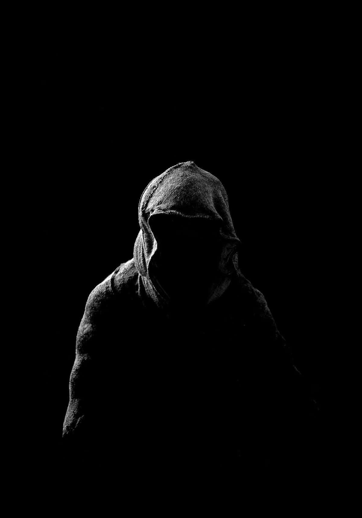 一個陰暗的戴頭巾人物站在黑暗中，微弱的光線勾勒出他們的形態。 — 詭異的GIF 壁紙