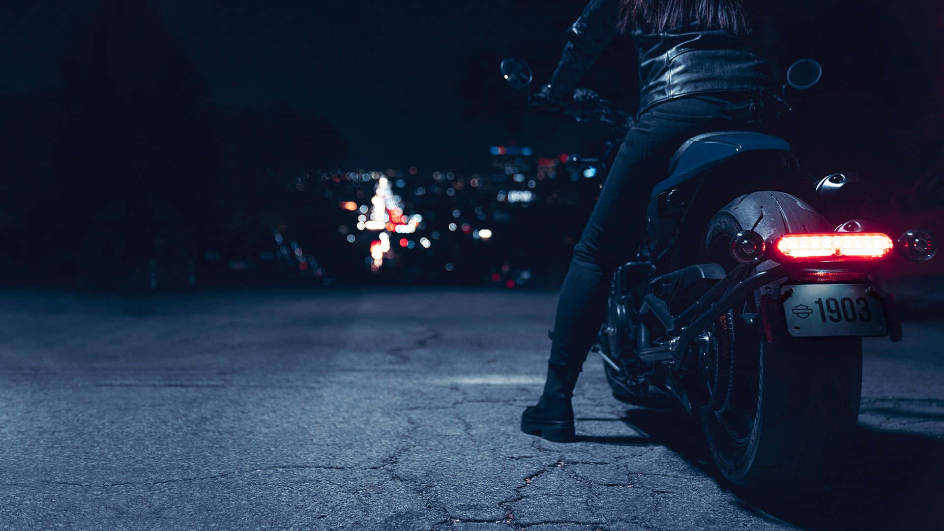 Harley Davidson HD 桌布 壁紙 — 一個孤獨的摩托車手穿著皮革裝備，坐在一輛紅色尾燈發光的摩托車上，背景是夜晚黑暗的城市天際線。