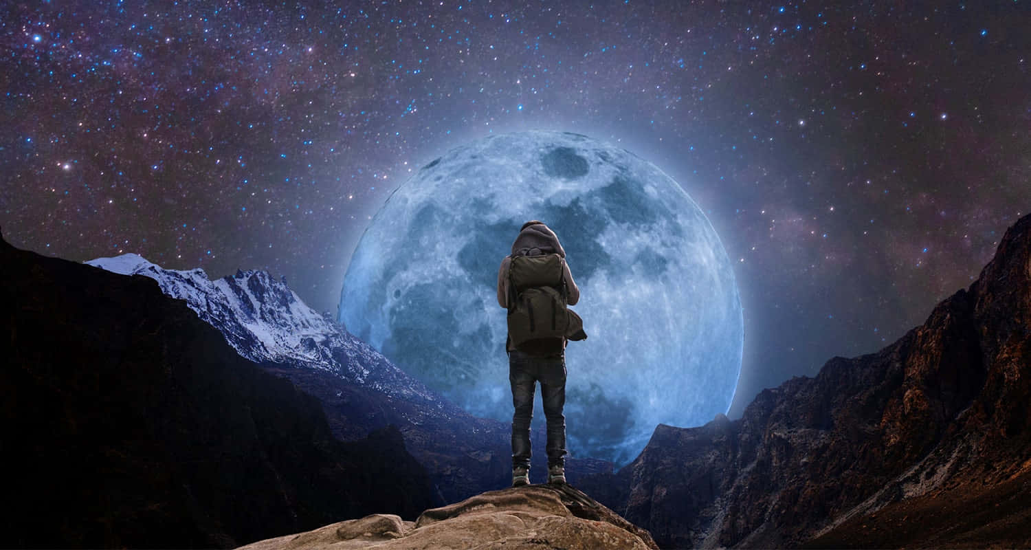 Dreaming 桌布 壁紙 — 一個孤獨的旅人站在山頂上，頭頂是巨大的藍色月亮和星空。