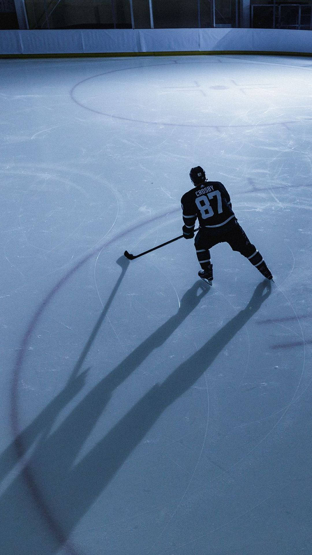 Cool Hockey 桌布 壁紙 — 一個孤獨的曲棍球運動員穿著黑色球衣號碼87，在戲劇性的聚光燈下站在冰場上，投射出長長的陰影。