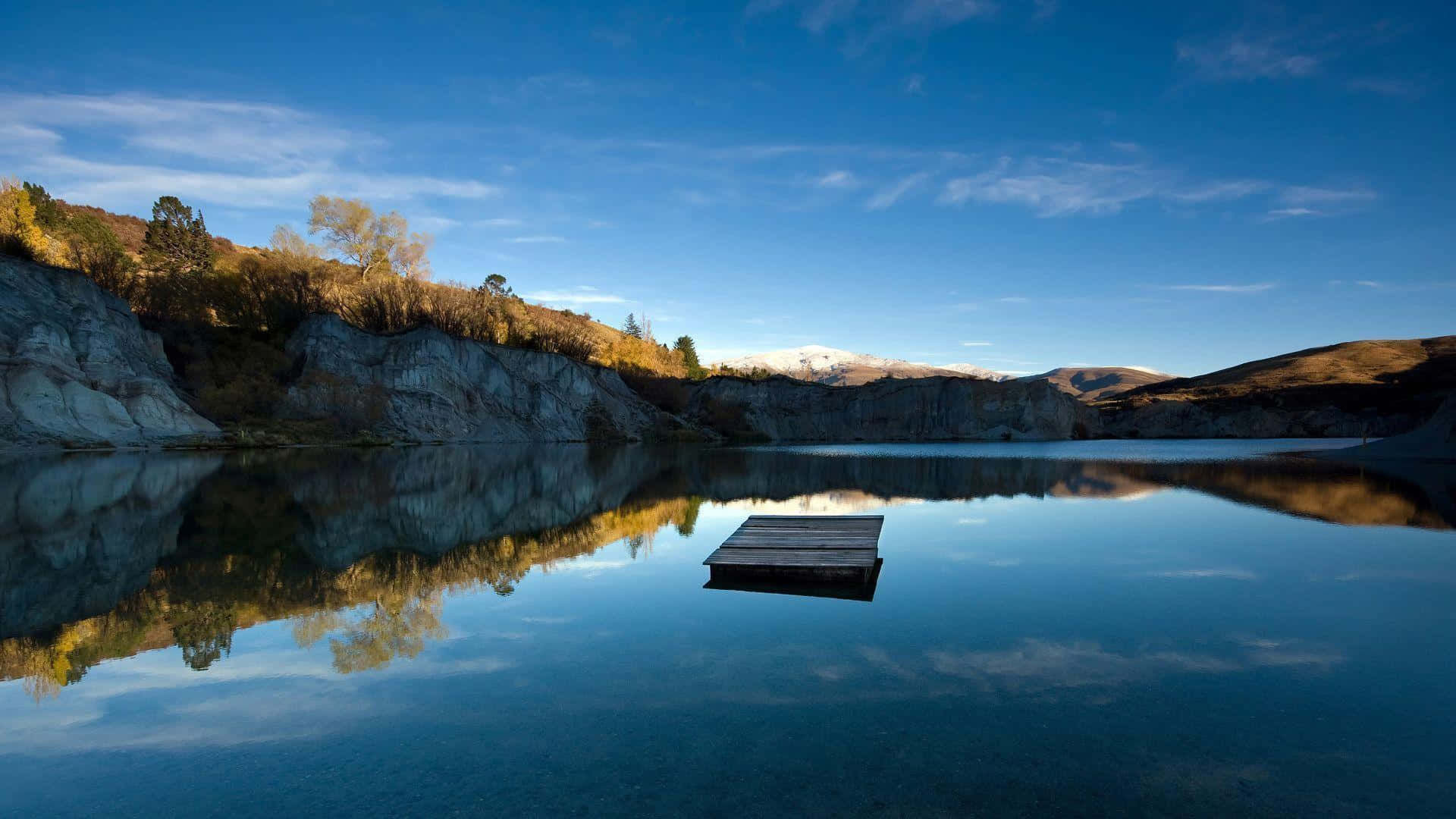 Lake 桌布 壁紙 — 一個孤獨的木碼頭漂浮在如鏡的湖面上，倒映著白雪覆蓋的山脈和秋色懸崖，天空清澈湛藍。
