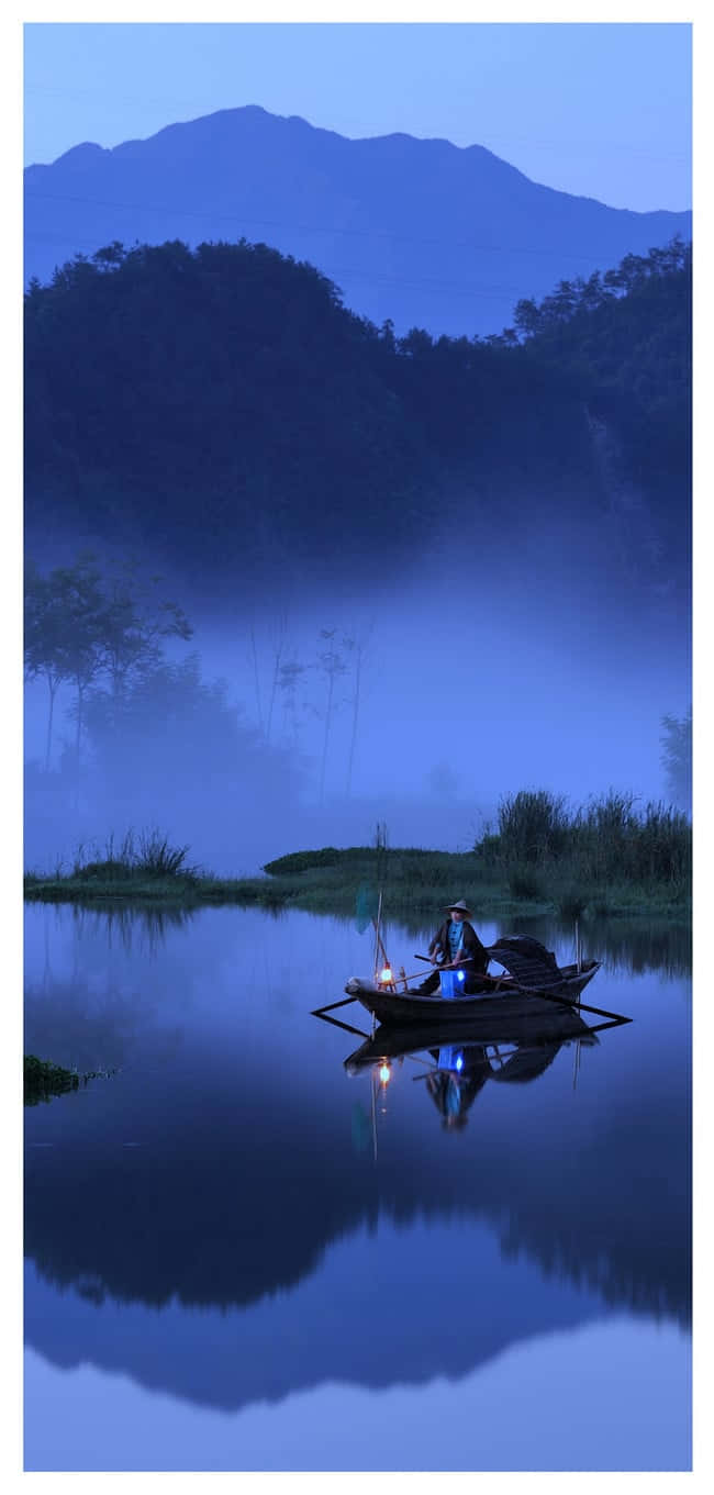 Fishing Phone 桌布 壁紙 — 一個孤獨的漁夫坐在小船裡，滑過霧氣瀰漫的暮色湖泊，平靜的水面倒映著山巒。