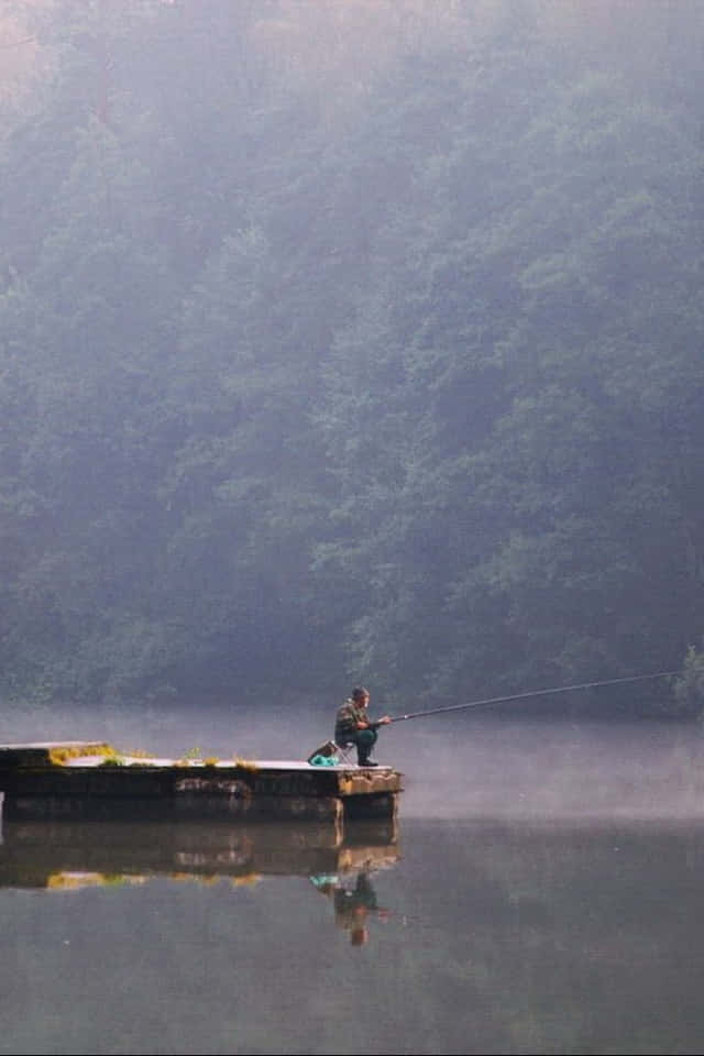 釣魚 桌布 壁紙 — 一個孤獨的漁夫坐在霧氣瀰漫的碼頭上，向被茂密森林環繞的平靜湖泊投下釣線。