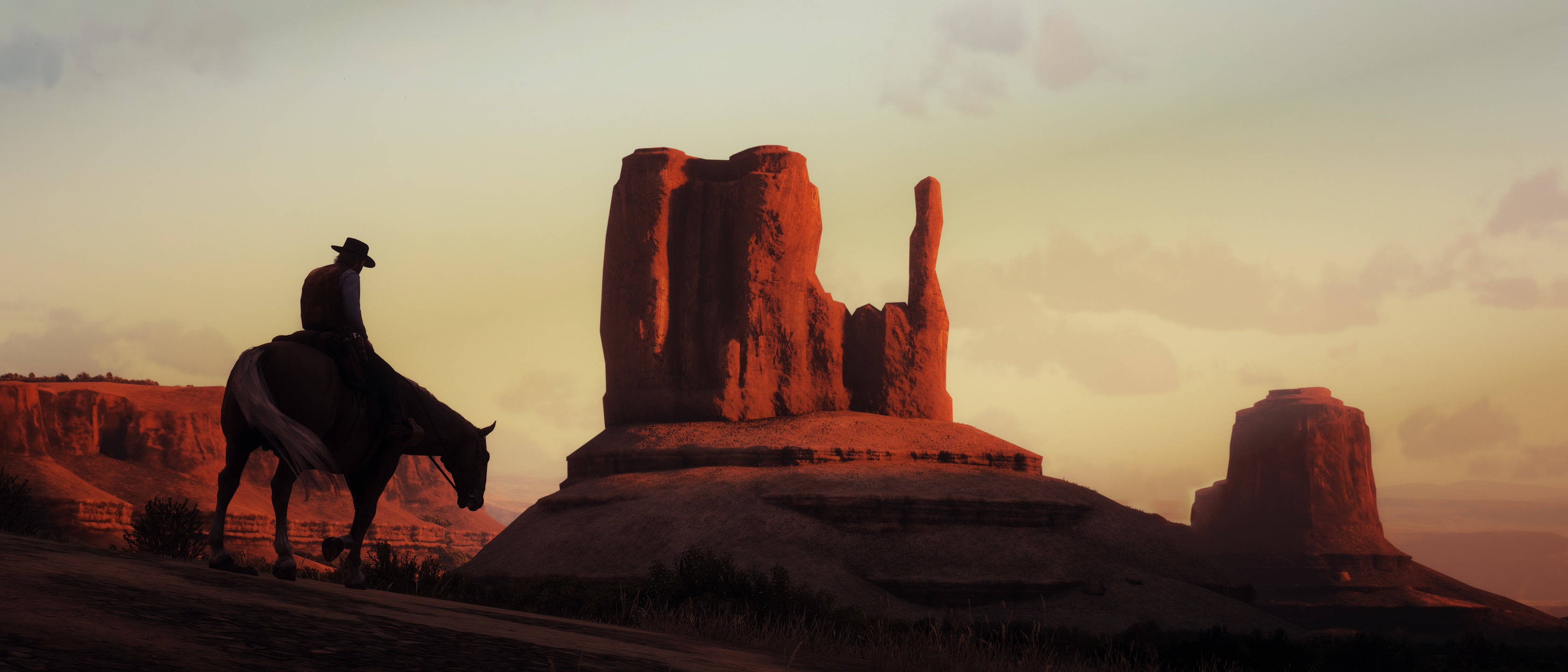 Red Dead Redemption 2 Desktop 桌布 壁紙 — 一個孤獨的牛仔騎在馬上，在高聳的紅色岩層旁邊，以燦爛的日落為背景形成剪影。
