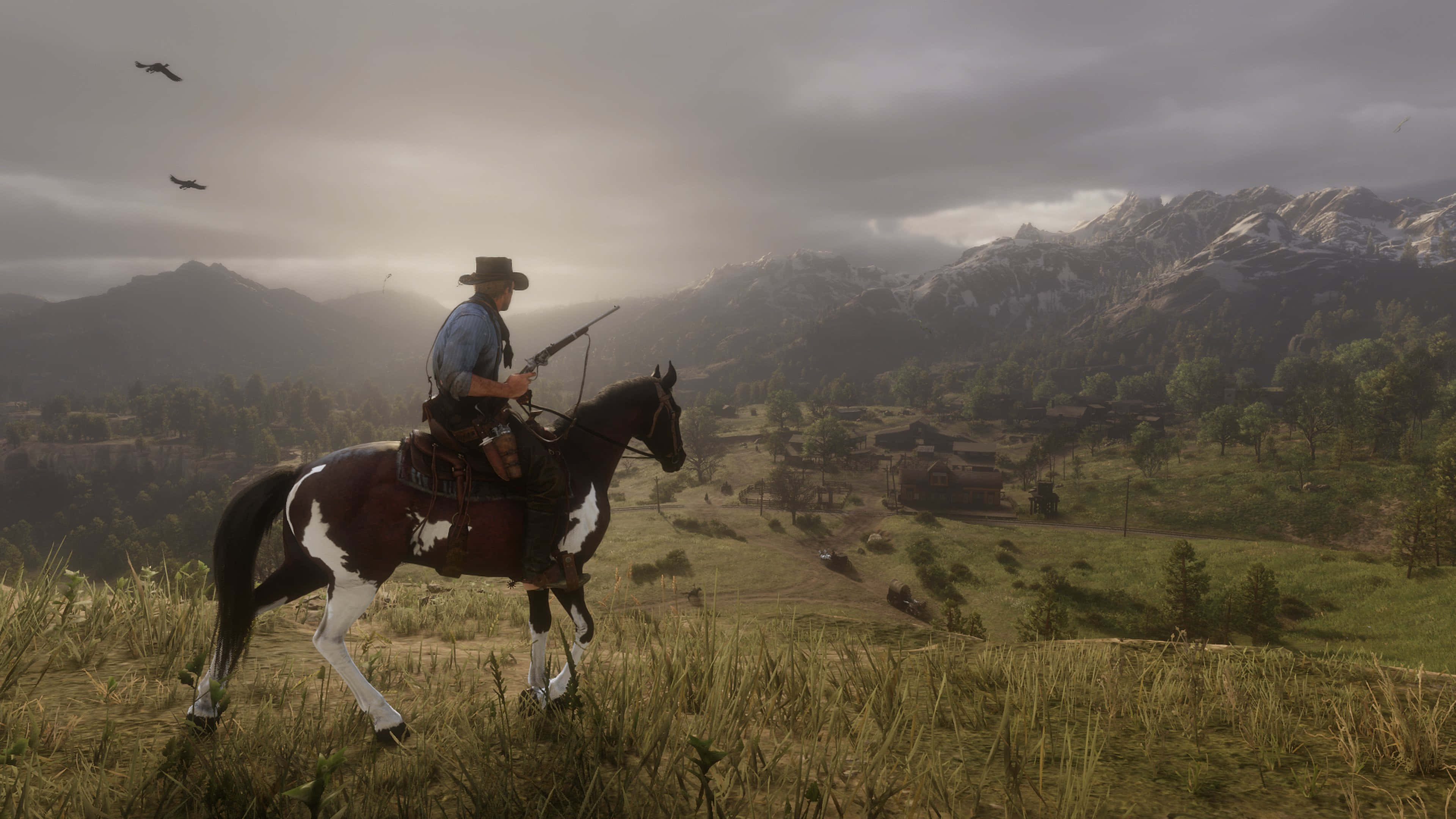 arthur morgan 桌布 壁紙 — 一個孤獨的牛仔騎著一匹花馬，穿過一片草地山丘，俯瞰著一個山谷，遠處有白雪覆蓋的山脈，天空多雲。