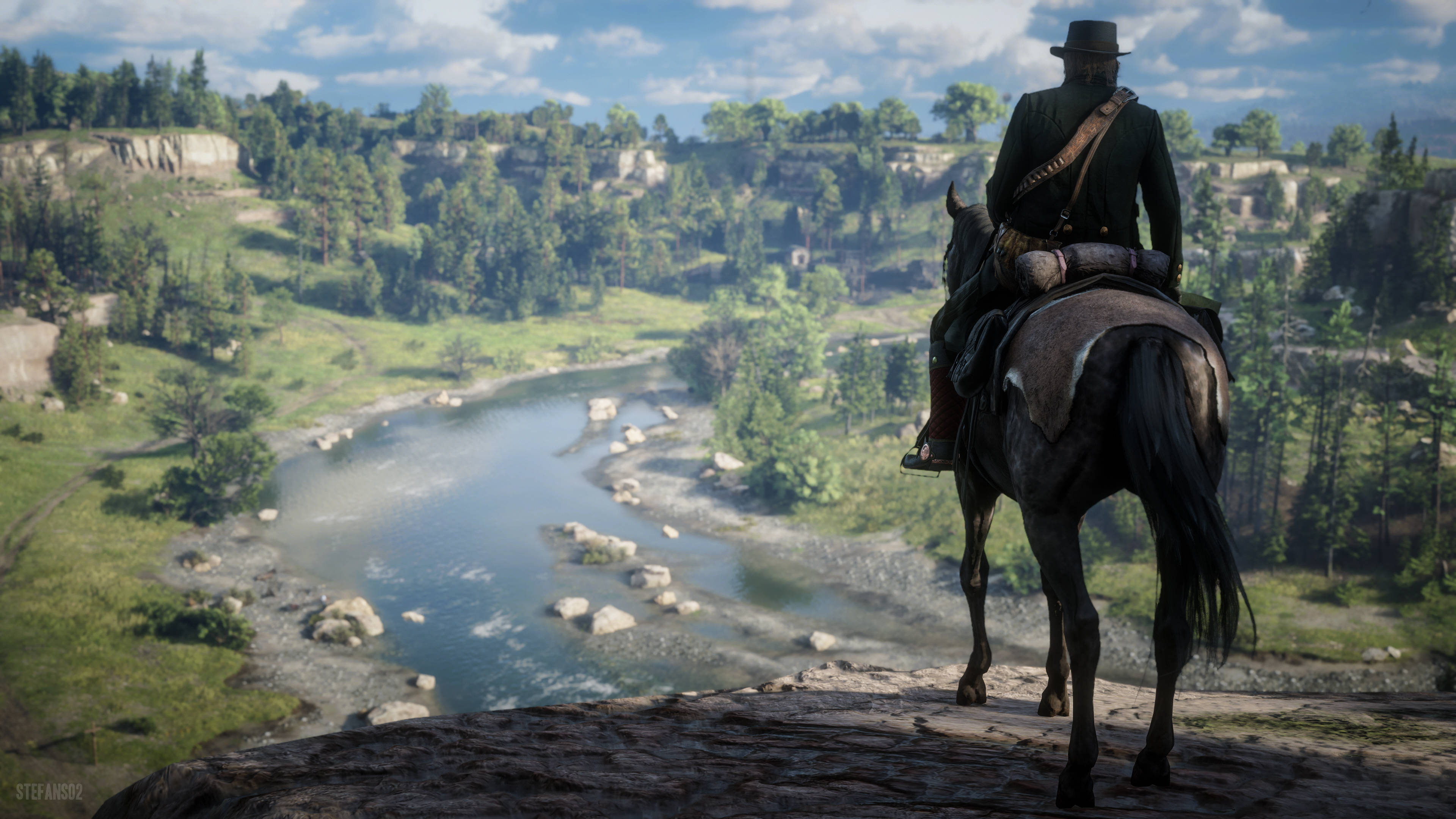 Red Dead Redemtion 2 桌布 壁紙 — 一個孤獨的牛仔騎著一匹黑馬，俯瞰著陽光普照的森林山谷中蜿蜒的河流，天空部分多雲。