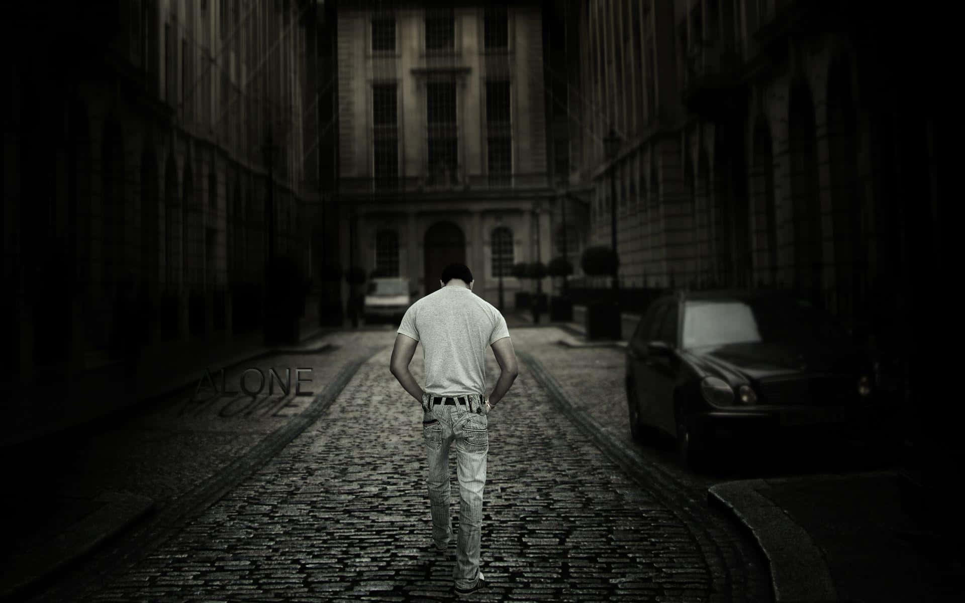 Alone 桌布 壁紙 — 一個孤獨的男人沿著一條狹窄的鵝卵石小巷走遠，兩旁是高樓大廈，燈光昏暗。