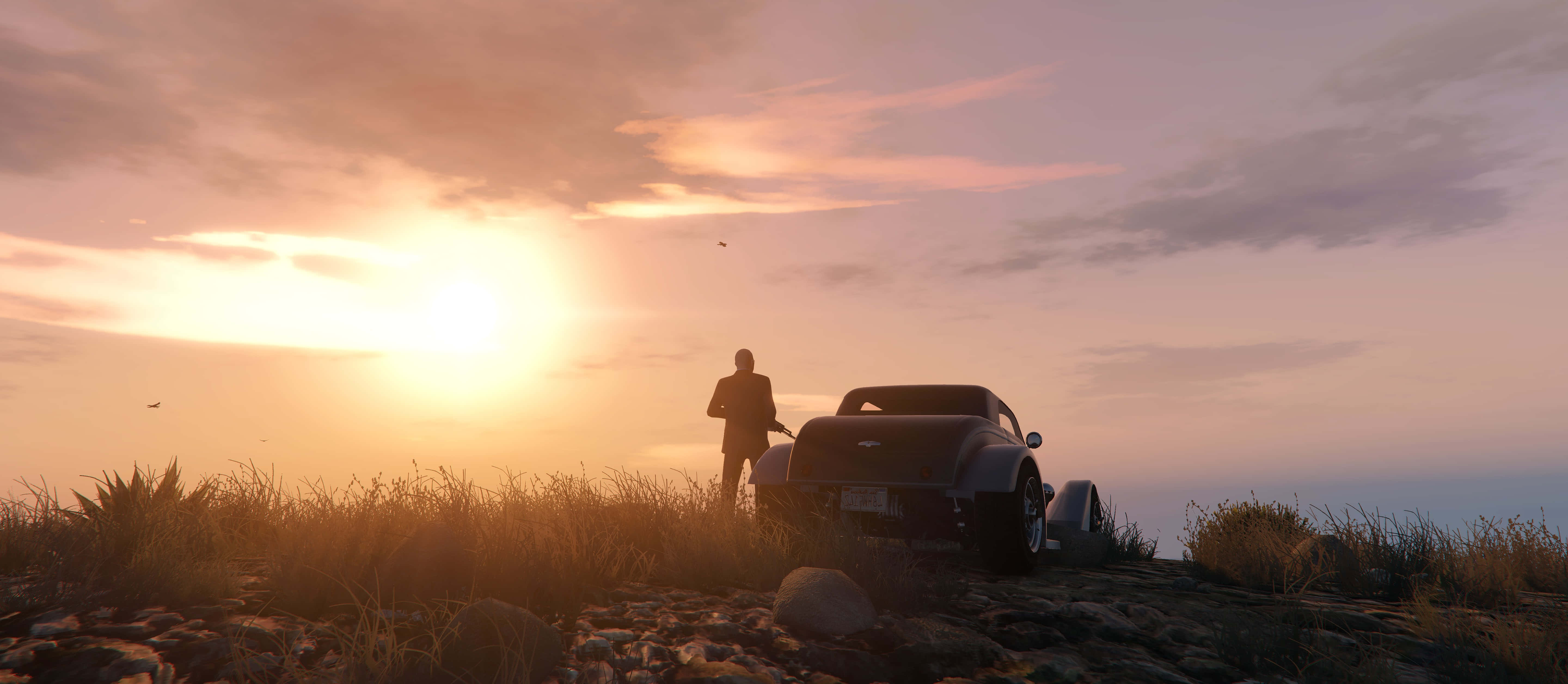 Grand Theft Auto V 桌布 壁紙 — 一個孤獨的男人站在一輛時尚的黑色跑車旁邊，在岩石山坡上，夕陽以溫暖的橙色和粉紅色調落下。