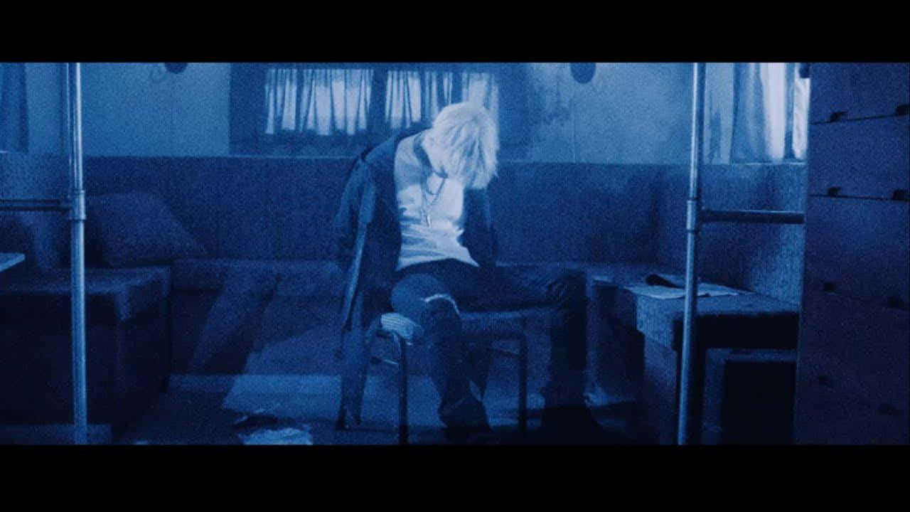 Agust D 桌布 壁紙 — 一個孤獨的白髮人癱坐在一張椅子上，房間內有昏暗的藍色燈光、雙層床和窗簾。