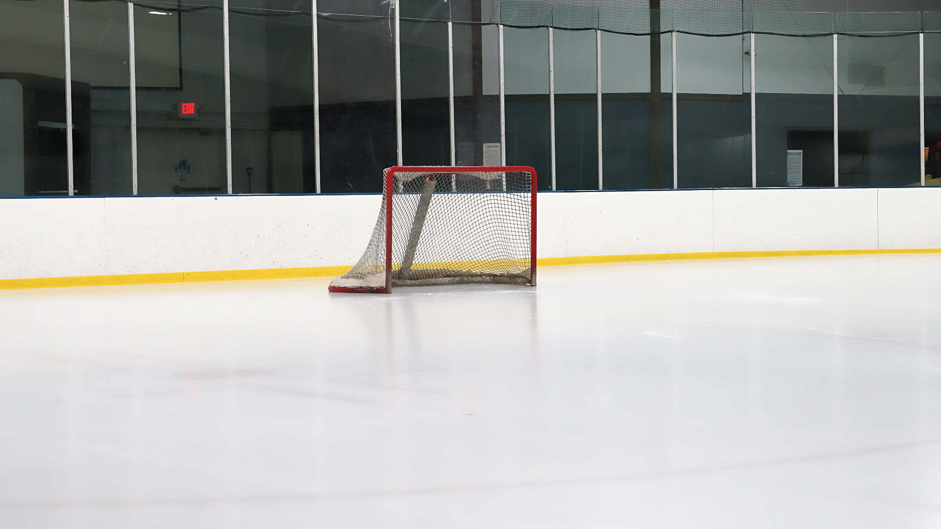 Ice Rink 桌布 壁紙 — 一個孤獨的紅色曲棍球球門矗立在明亮的室內燈光下的純白冰場上。