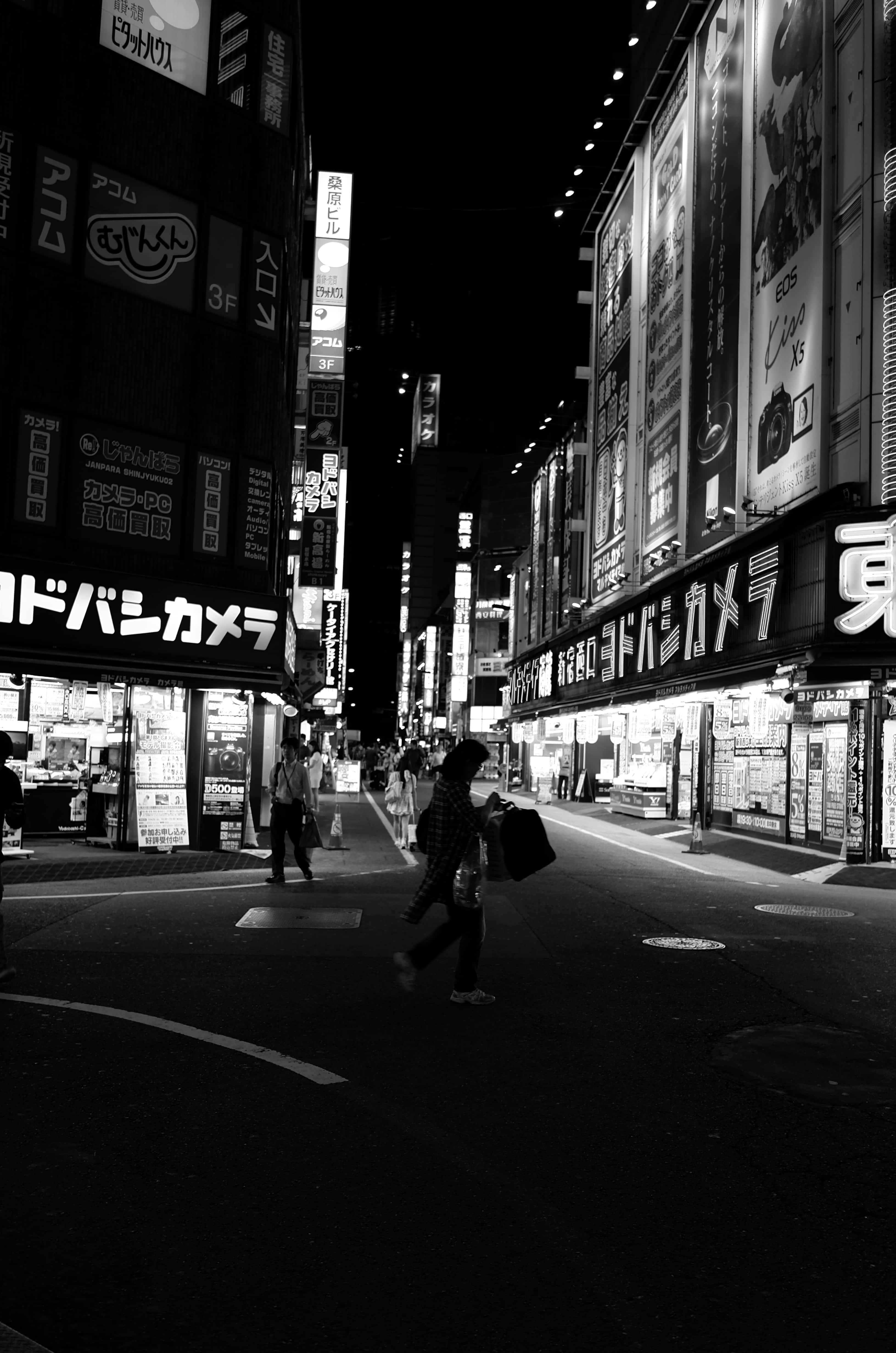 日本黑白 桌布 壁紙 — 一個孤獨的行人在夜晚穿過霓虹燈照亮的東京街道，高聳的廣告牌和發光的標誌投下鮮明的陰影。