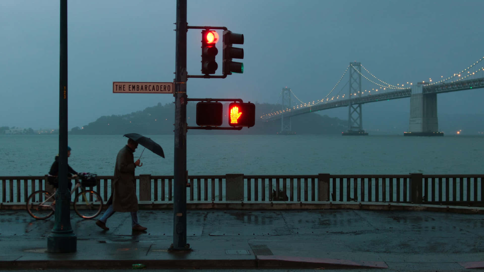 Stop Light 桌布 壁紙 — 一個孤獨的行人撐著雨傘，在霧氣瀰漫的碼頭走過一個亮著紅燈的交通號誌，遠處有一座橋，天空灰濛濛。