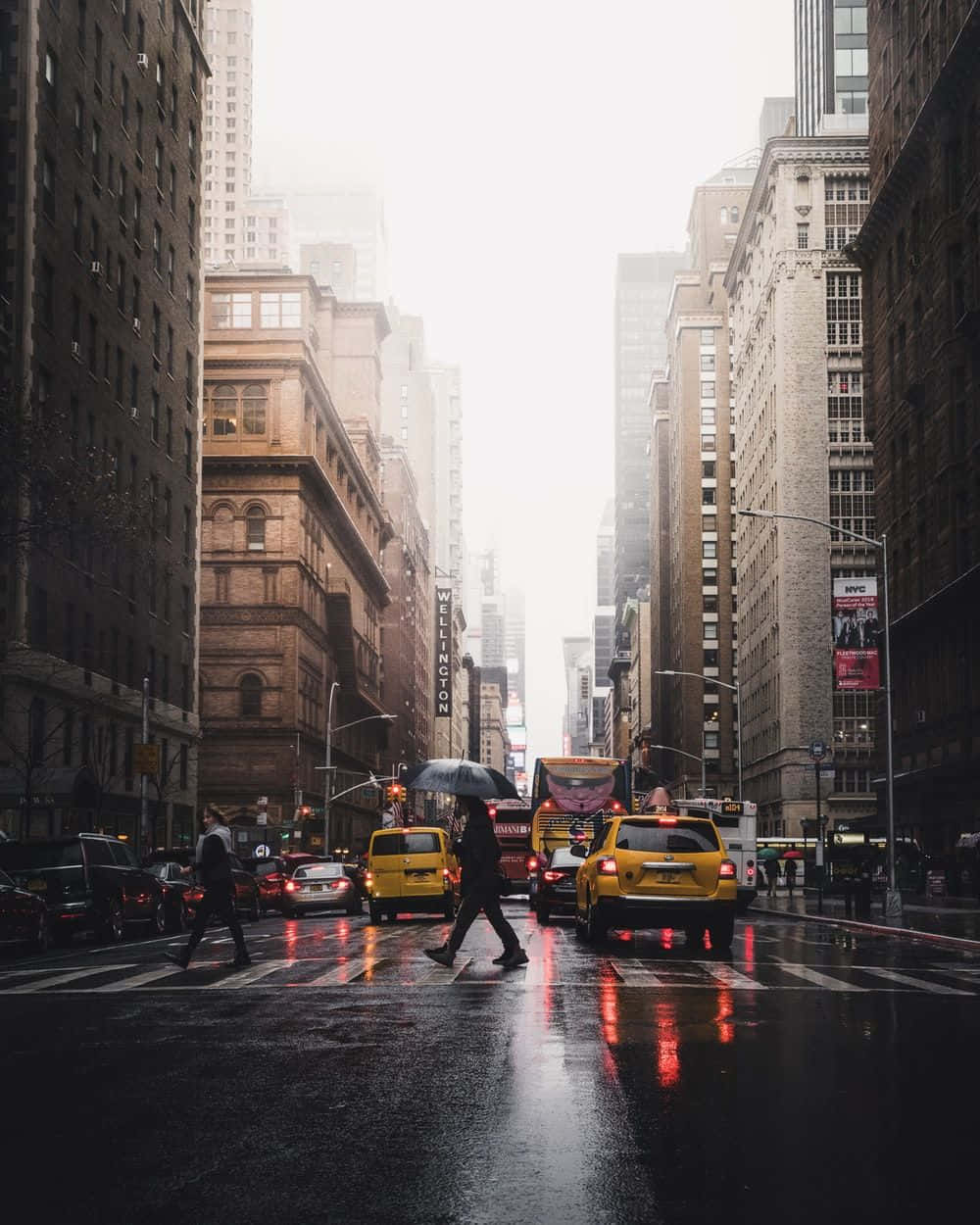 Old New York City 桌布 壁紙 — 一個孤獨的行人撐著雨傘，穿過一條被雨水浸濕的城市街道，兩旁是高聳的建築物和黃色的計程車。