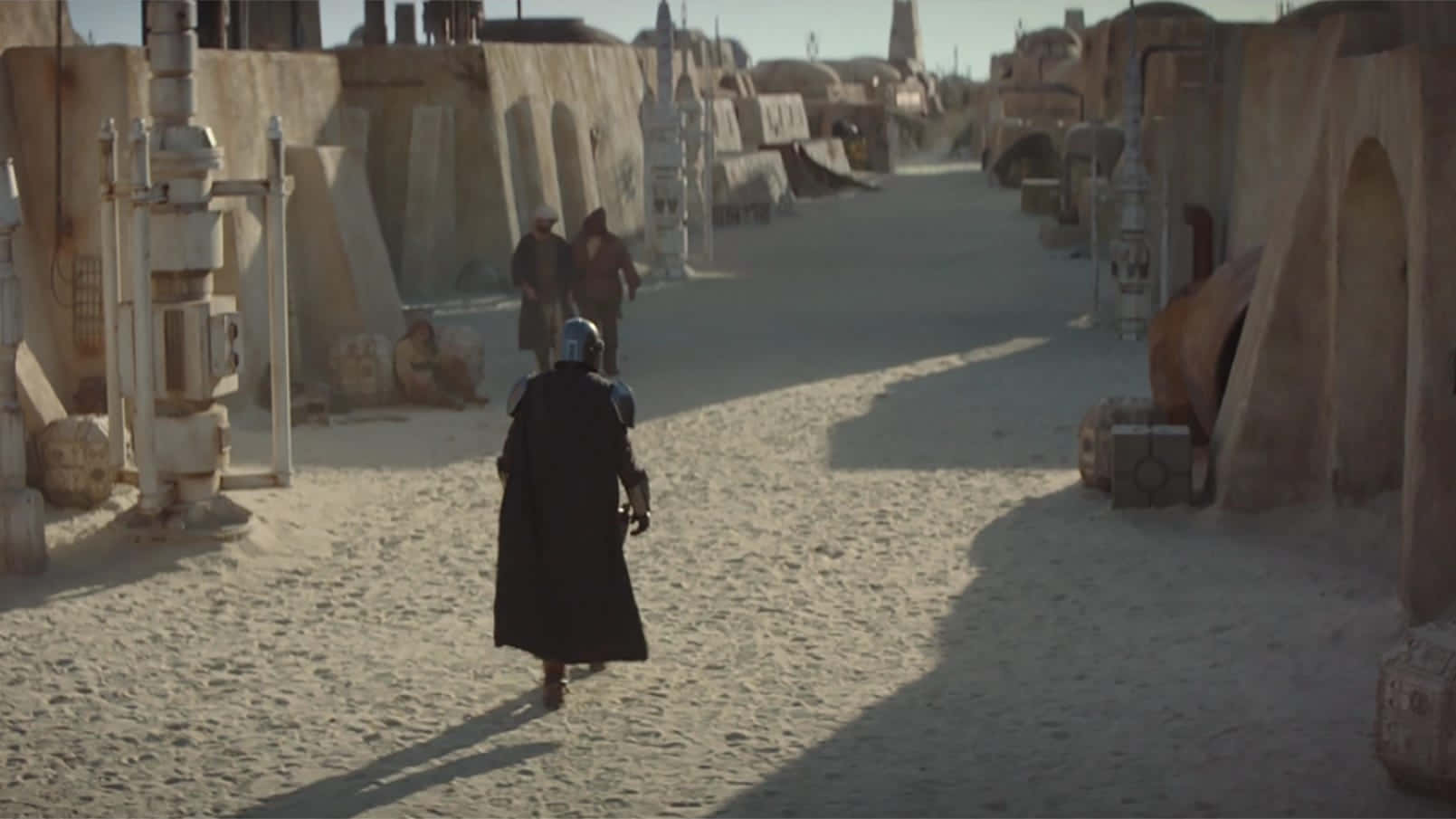 Tatooine 桌布 壁紙 — 一個孤獨的裝甲人物走在沙漠小鎮陽光明媚的沙質街道上，街道上有風化的石頭建築和遠處的人物。