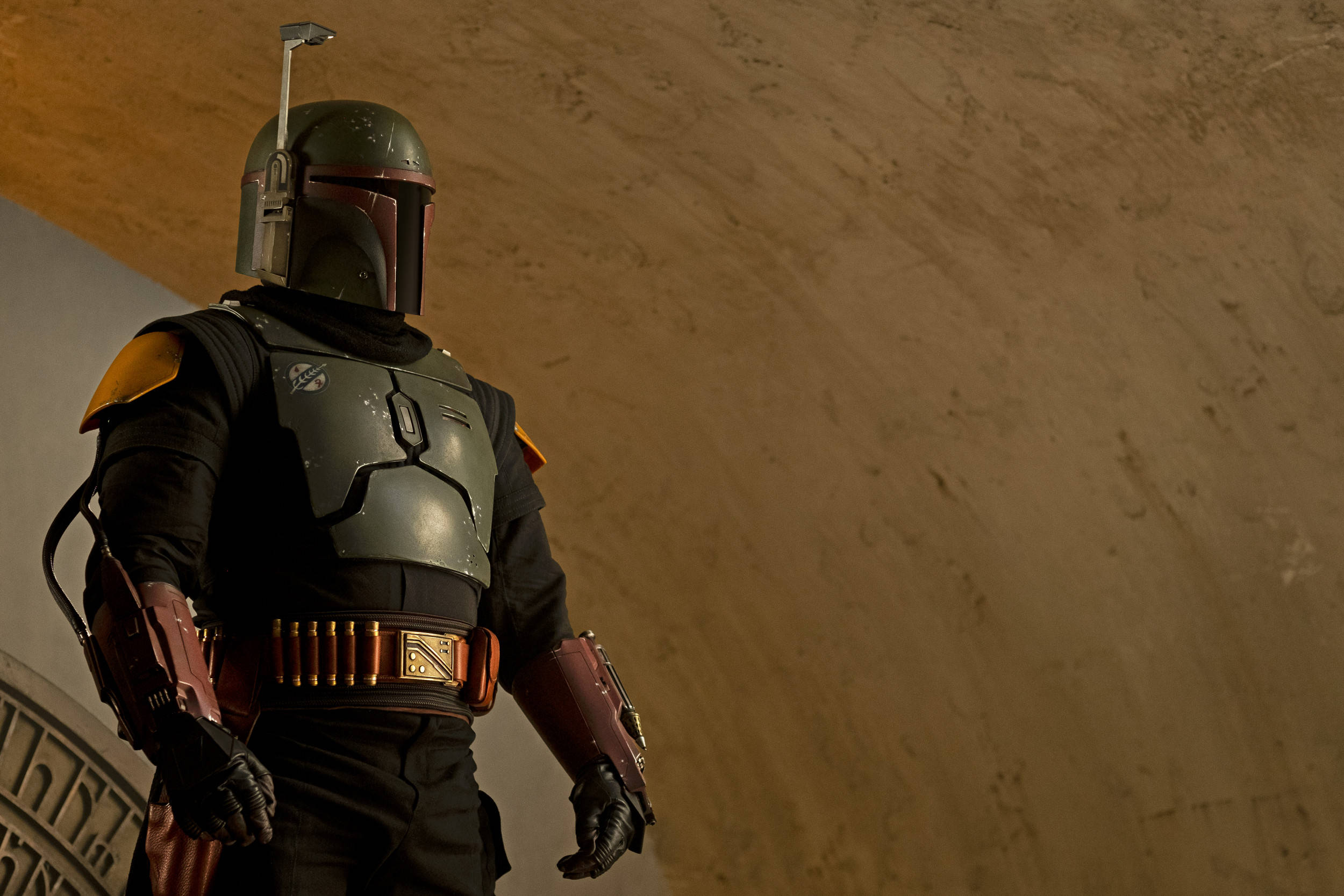 Boba 桌布 壁紙 — 一個孤獨的賞金獵人身穿風化盔甲，站在燈光昏暗、牆壁有紋理的走廊中。