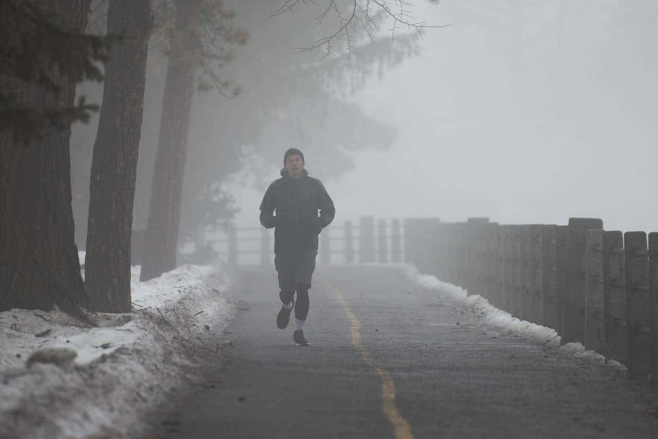 Exercise 桌布 壁紙 — 一個孤獨的跑者穿著深色夾克，在霧氣瀰漫的冬日道路上奔馳，路邊鋪滿積雪和光禿禿的樹木。