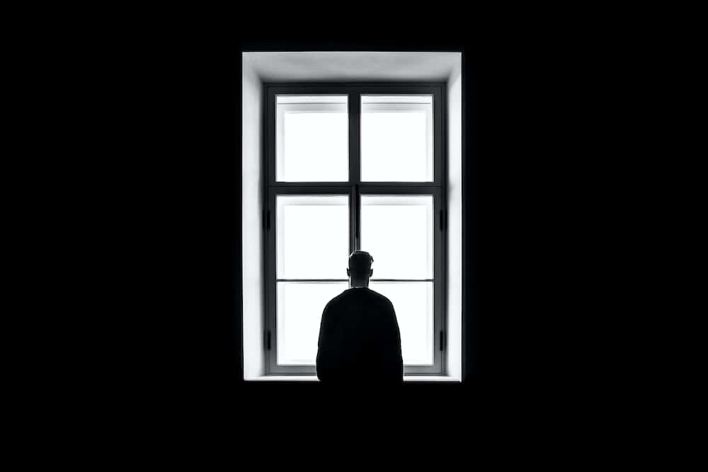 Depressing Profile 桌布 壁紙 — 一個孤獨的身影以剪影形式站在一個被深邃黑暗框住的明亮窗戶前，形成強烈對比。