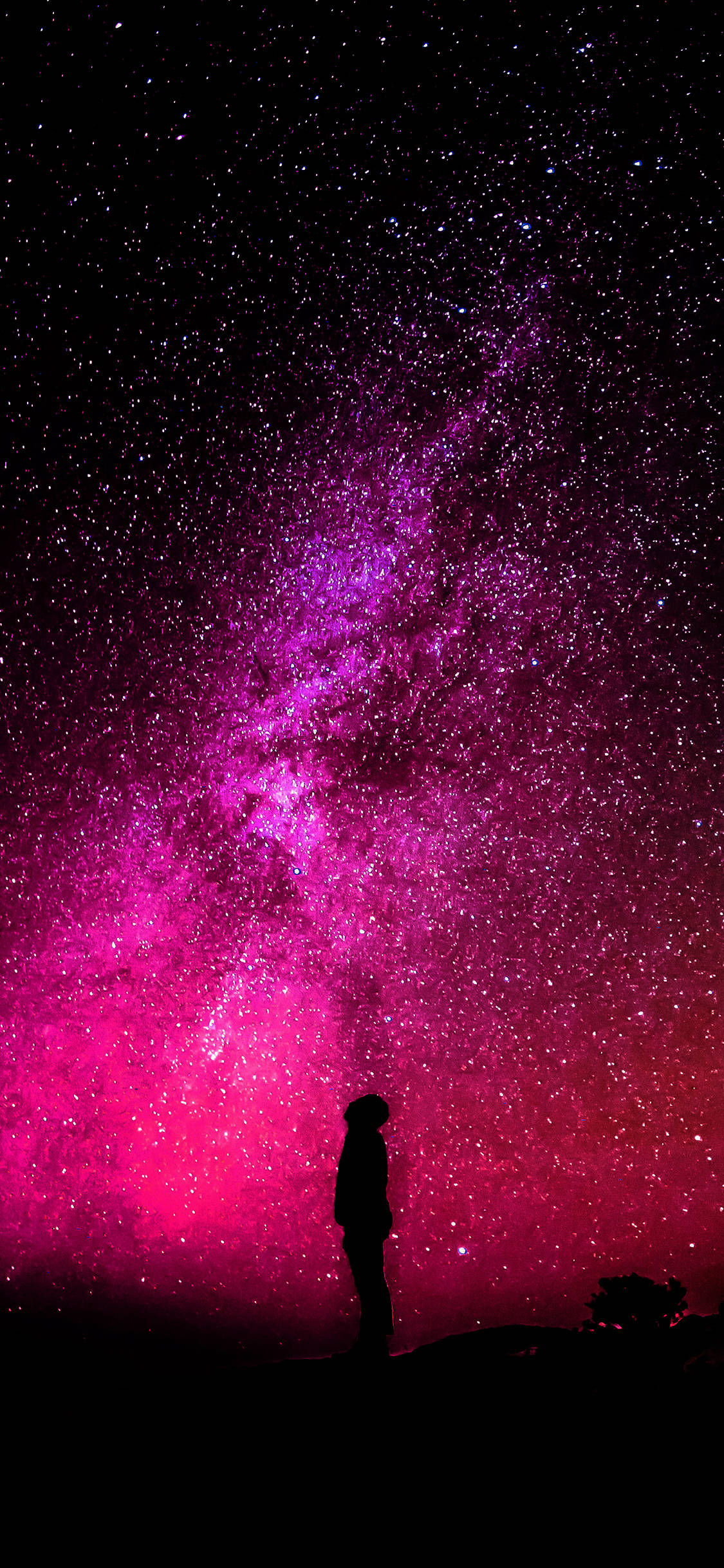 Galaxy iPhone 桌布 壁紙 — 一個孤獨的身影在令人嘆為觀止的粉紅色和紫色銀河下，敬畏地站在繁星點點的夜空下。