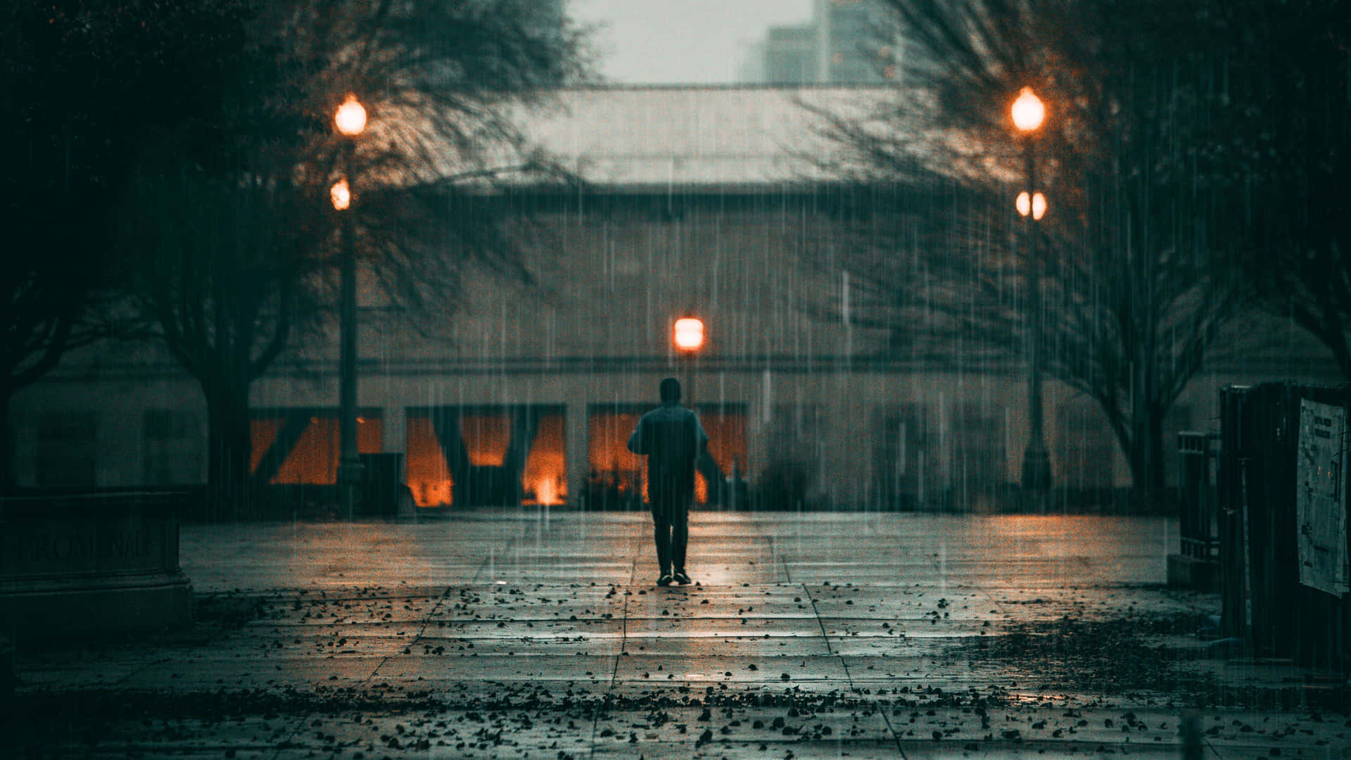 Sad Face 桌布 壁紙 — 一個孤獨的身影在傾盆大雨中走過濕漉漉的城市廣場，廣場被溫暖發光的街燈照亮。
