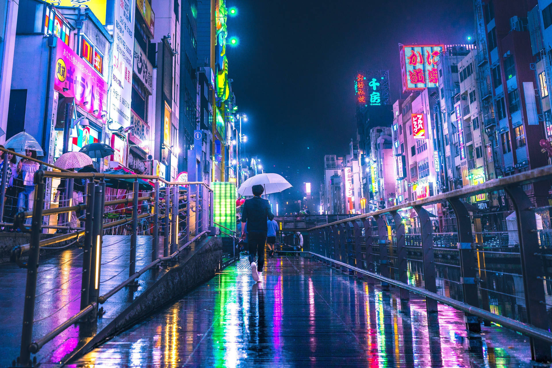 夜晚，一個人在發光的霓虹招牌下撐著傘走在濕漉漉的橋上。