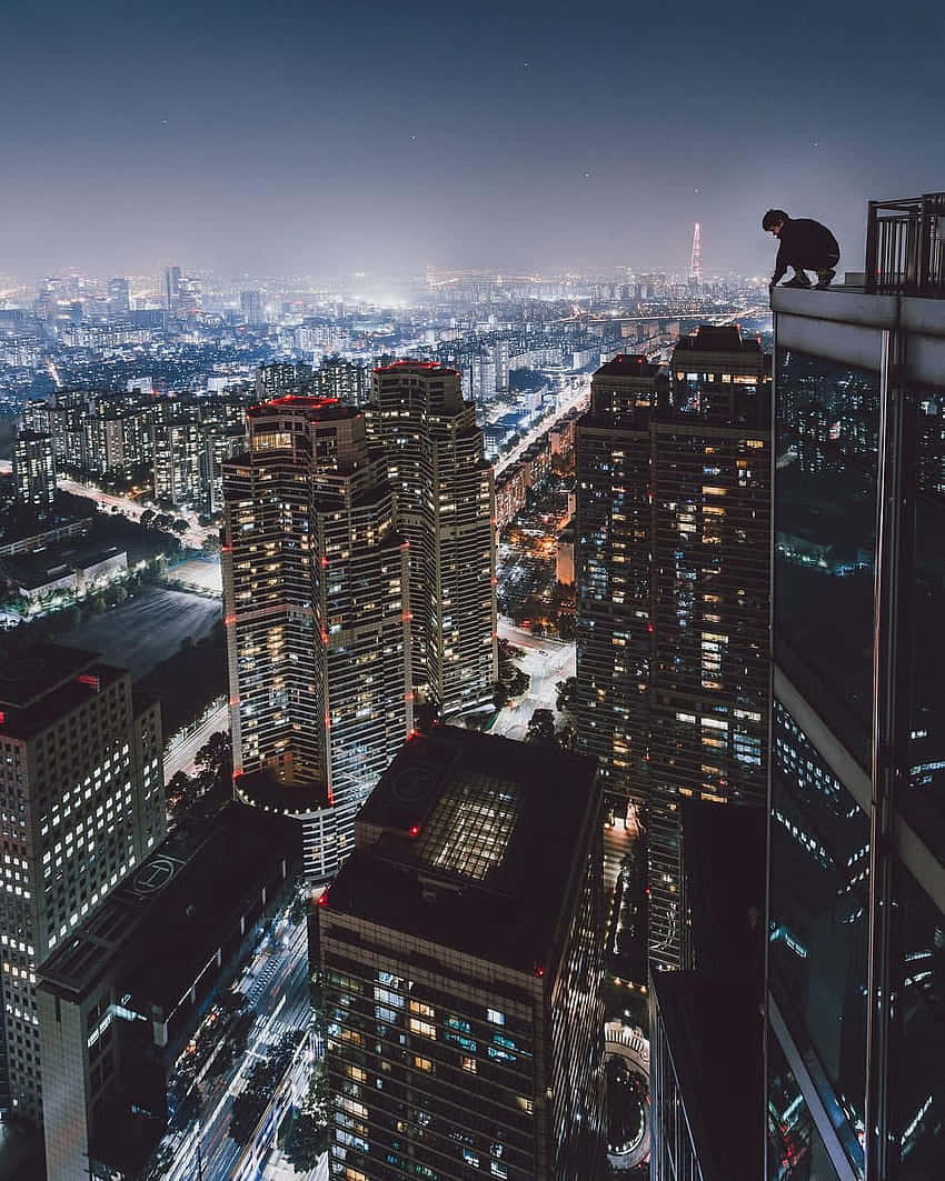 Rooftop 桌布 壁紙 — 一個孤獨的身影在夜晚棲身於摩天大樓頂端，俯瞰著霓虹燈和星空下廣闊的城市景觀。