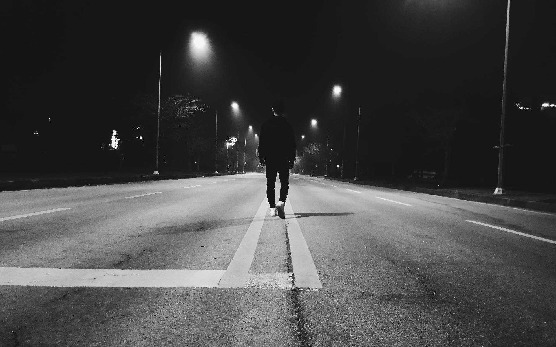 獨自一人 桌布 壁紙 — 一個孤獨的身影在夜晚沿著一條荒涼的街道行走，被路燈照亮，投下長長的影子。