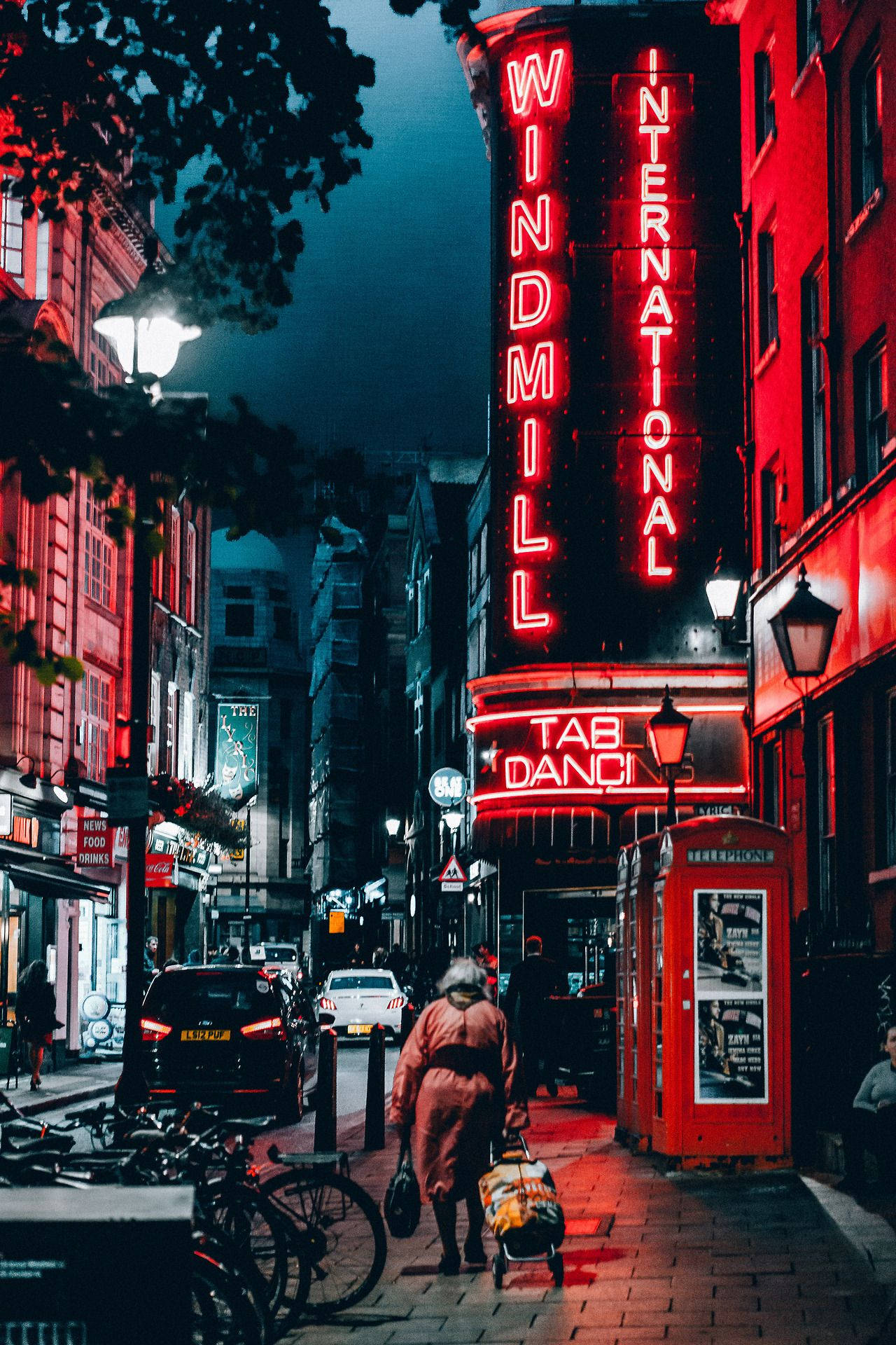 復古美學 桌布 壁紙 — 一個孤獨的身影在夜晚沿著倫敦一條狹窄的街道行走，被風車劇院充滿活力的紅色霓虹燈招牌照亮。