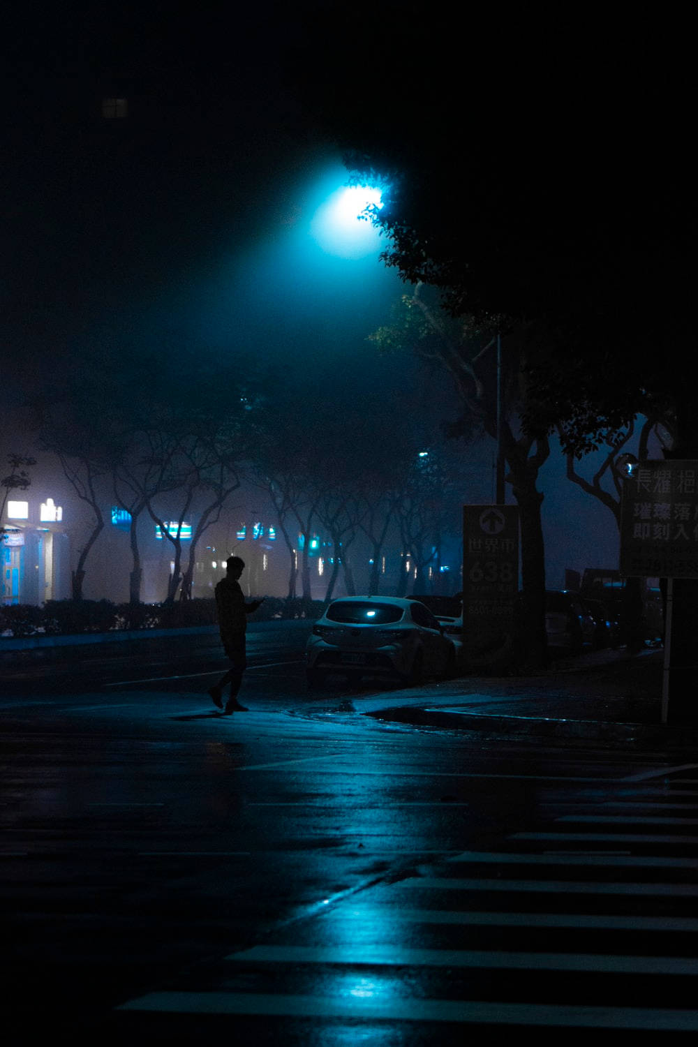 黑夜 桌布 壁紙 — 一個孤獨的身影在夜晚濕漉漉的城市街道上行走，頭頂只有一盞發出藍光的街燈，投下長長的影子。