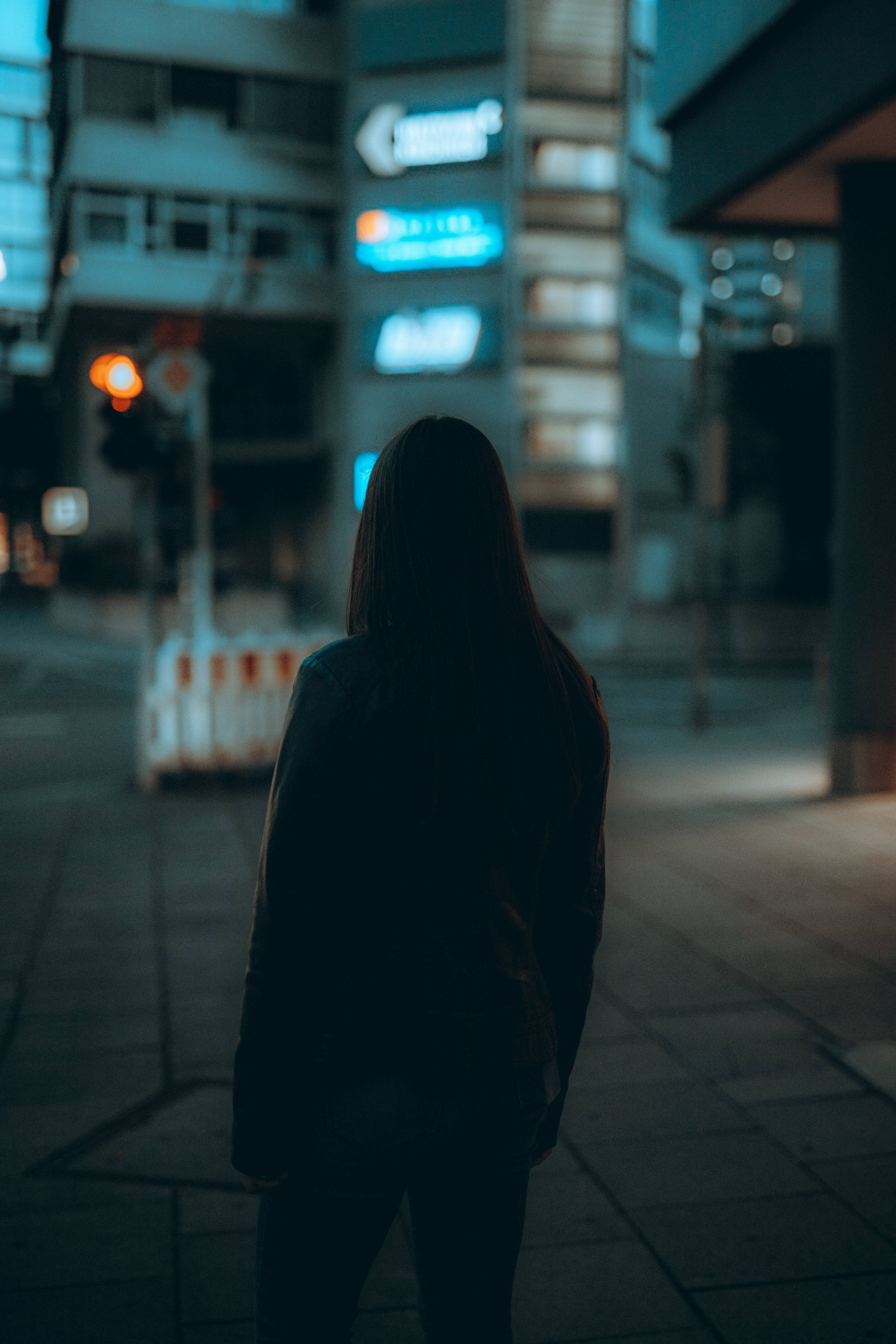 Woman 桌布 壁紙 — 一個孤獨的身影在夜晚的城市人行道上呈現剪影，仰望發光的霓虹燈招牌和模糊的城市燈光。