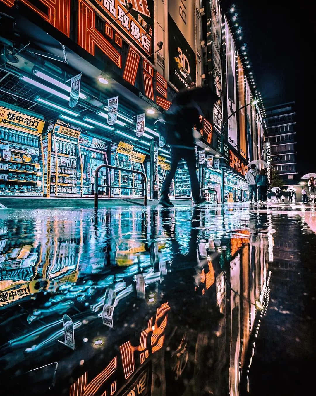 Street Light 桌布 壁紙 — 一個孤獨的身影在夜晚穿過東京一條霓虹燈閃爍的小巷，他們的剪影映照在雨水浸濕的柏油路上，散發著電光藍和橙色的光芒。