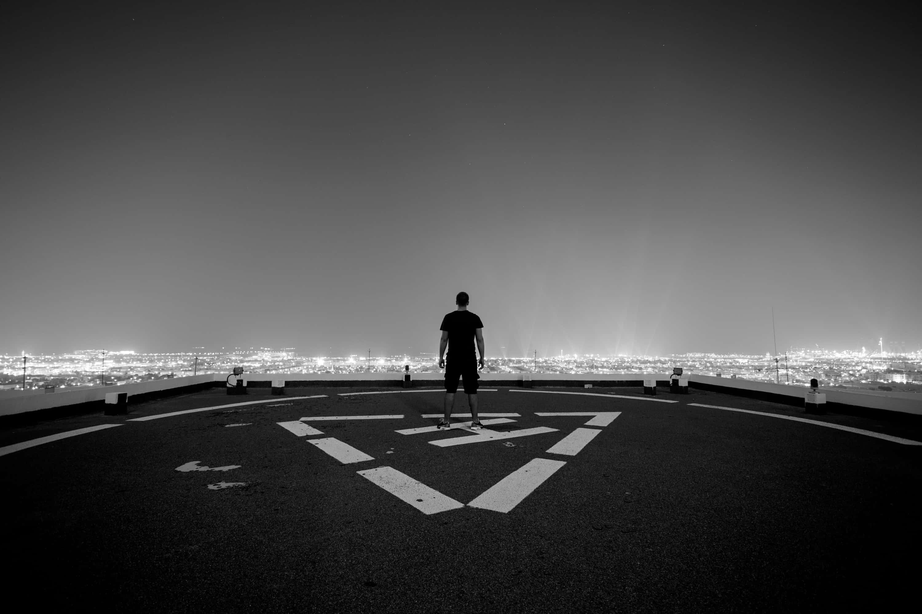 Rooftop 桌布 壁紙 — 一個孤獨的身影在夜晚站在屋頂上，俯瞰著被無數燈光照亮的廣闊城市景觀。
