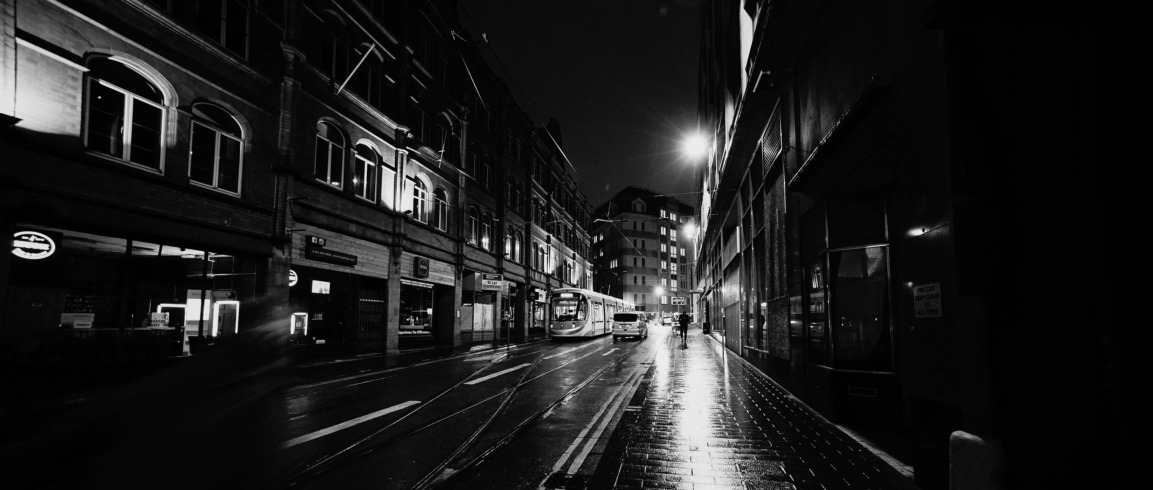 Birmingham 桌布 壁紙 — 一個孤獨的身影在夜晚行走在一條濕漉漉的黑白城市街道上，被路燈照亮，燈光反射在路面上。